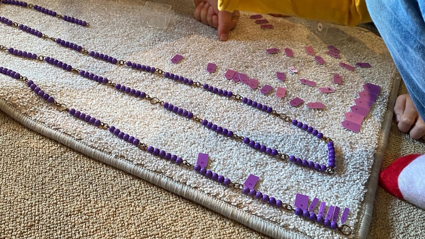 A long chain of purple beads is laid out on a mat, with purple number arrows being arranged.