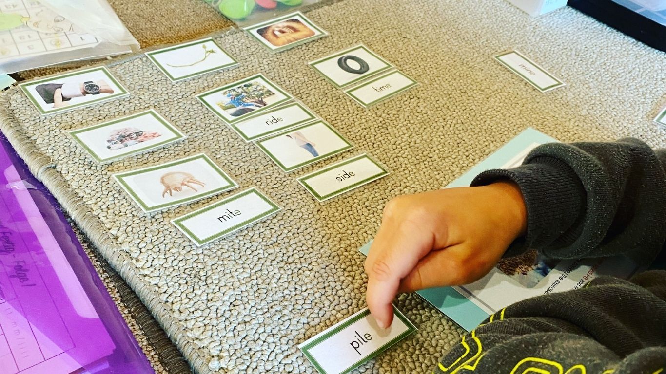 Small pictures and labels lie on a mat. The cards have a green edge and a finger can be seen at the bottom pointing to one word that is yet to be matched.