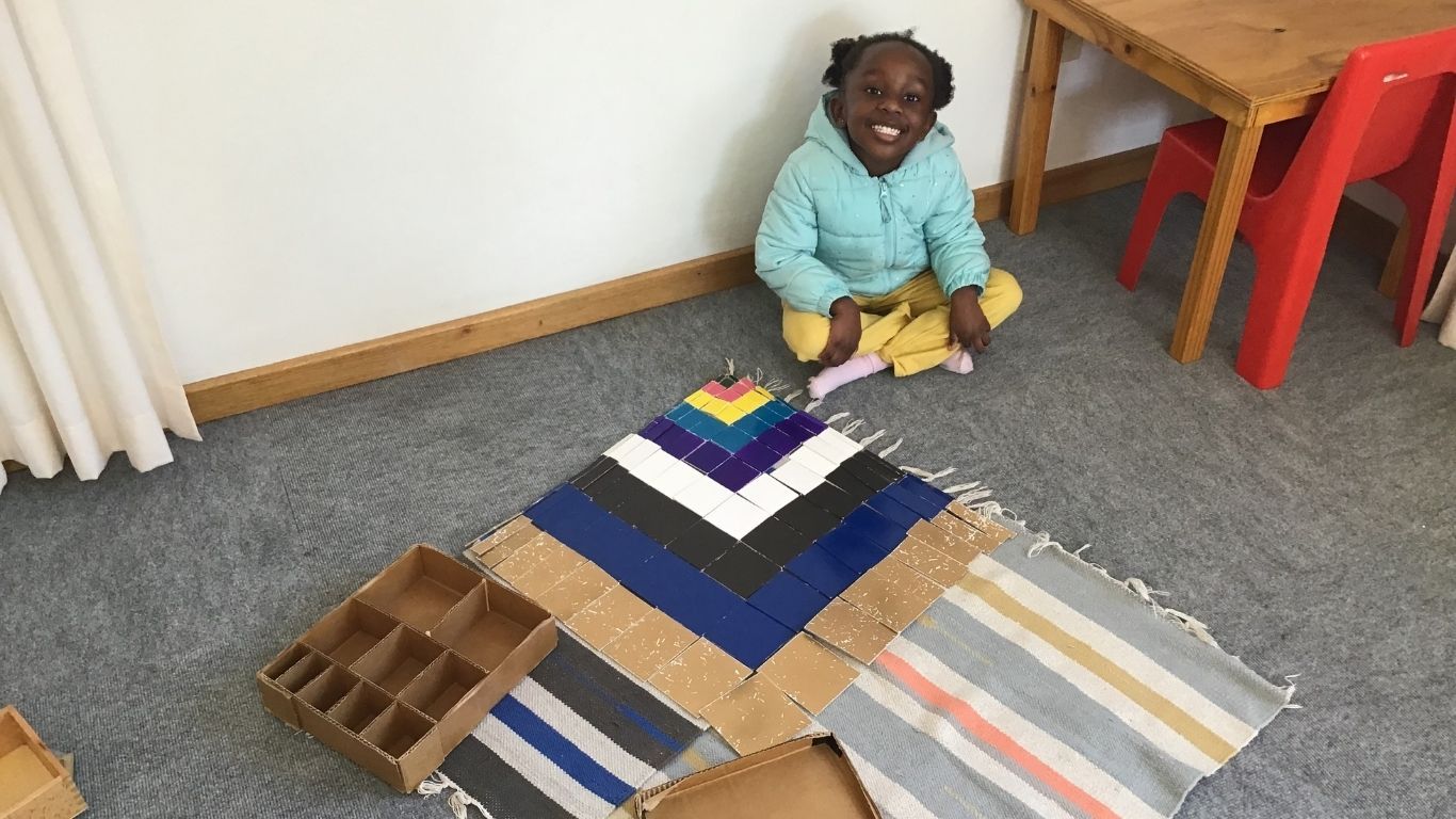 A girl sitting behind a completed puzzle of the times tables in different colours.