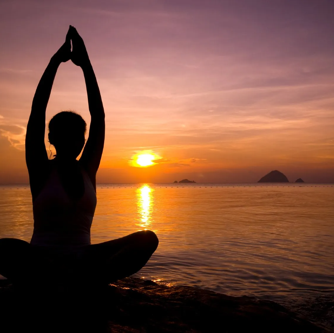 une personne assise en lotus bras en l'air face à un coucher de soleil
