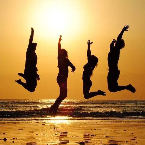 4 personnes sautent sur le sable devant la mer au coucher de soleil