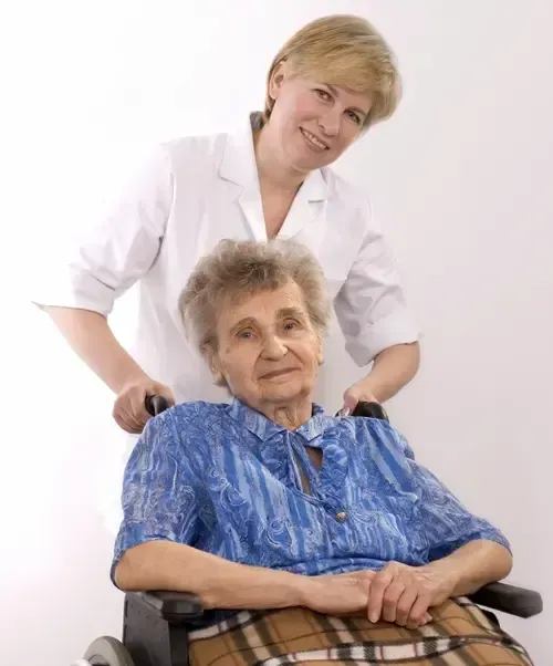 Oma sitzt im Rollstuhl und Pflegerin steht hinter IHR