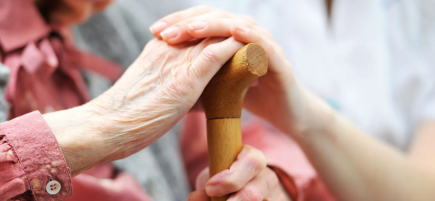 Oma hält Ihren Stock und die Pflegerin legt Ihre Hand darauf 2