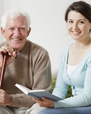 Oma sitzt im Rollstuhl und ist mit einer Decke und Blickt zur Pflegerin