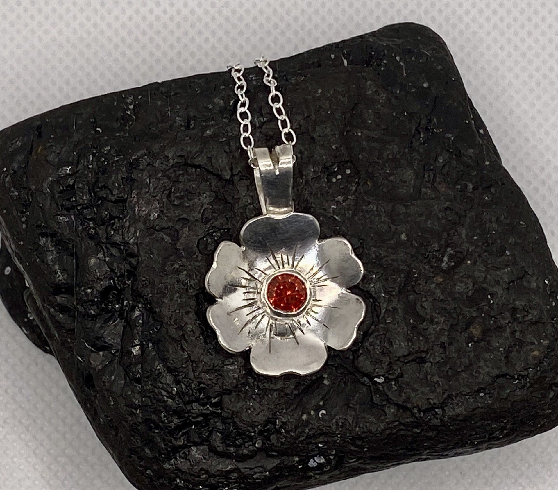 A silver flower pendant with red stone
