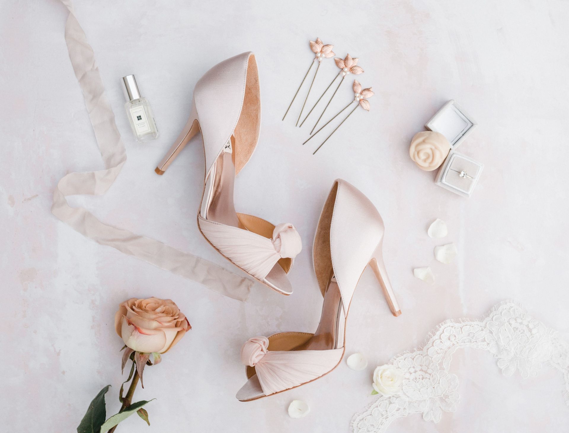 Pink wedding details flat lay including women's pink shoes perfume, and a wedding ring
