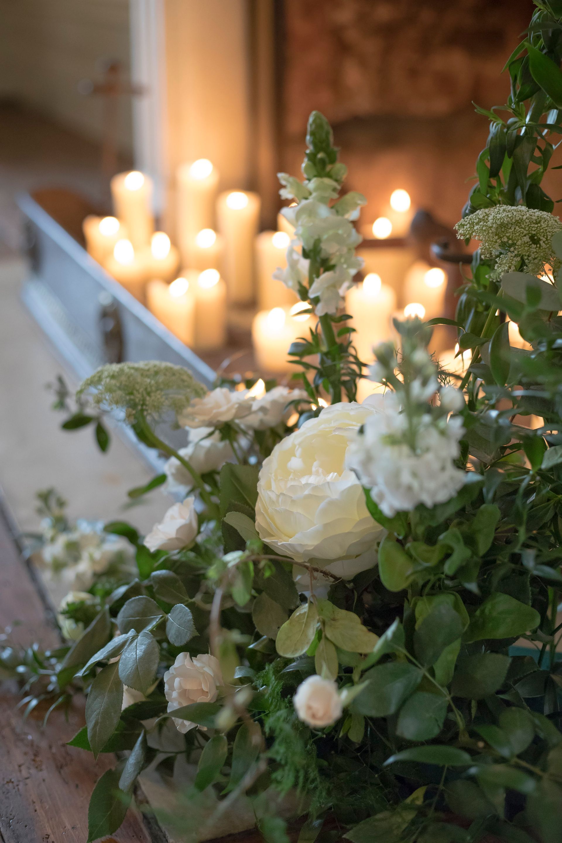A fireplace filled with cream lit candles with white rose and anemones decorating it