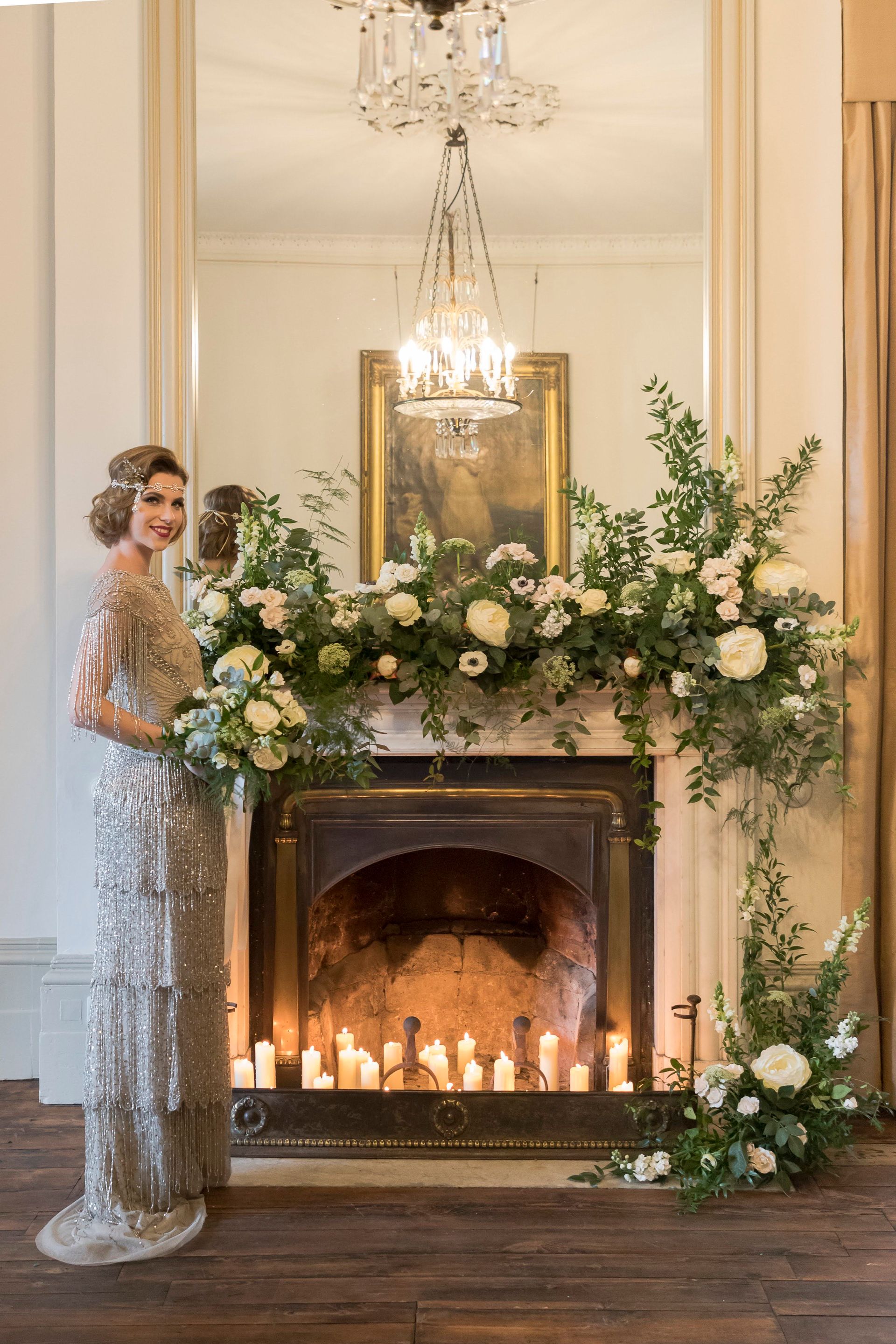 Gatsby inspired bride standing by fire place decorated with ivory flowers and lit candles