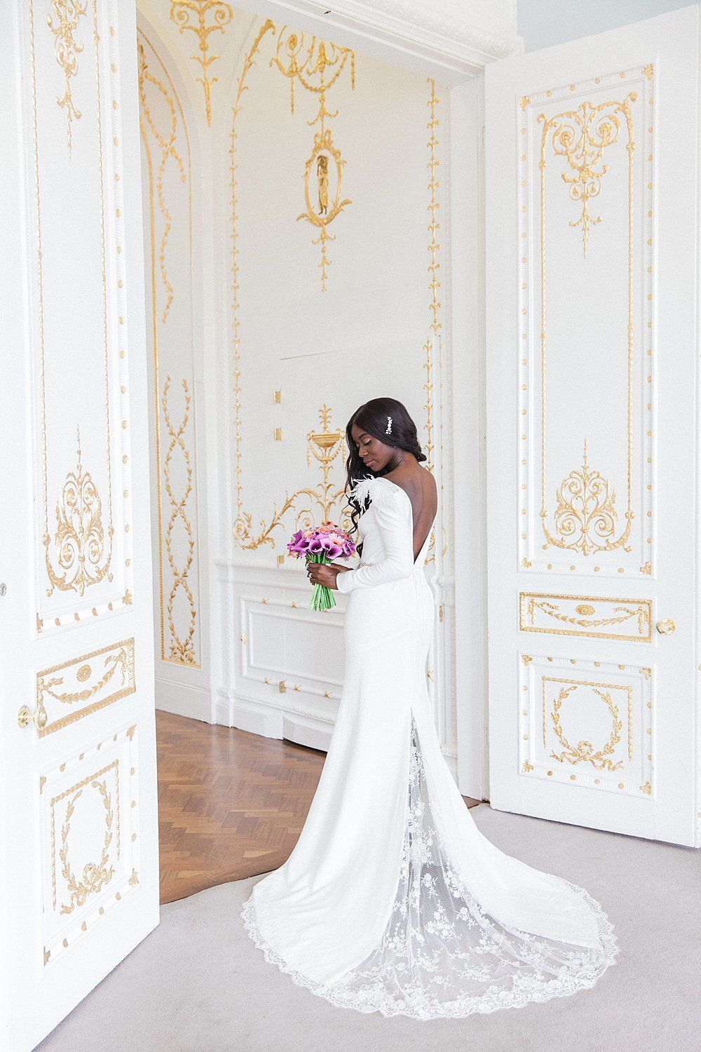 Bride standing displaying back of wedding dress with long lace train