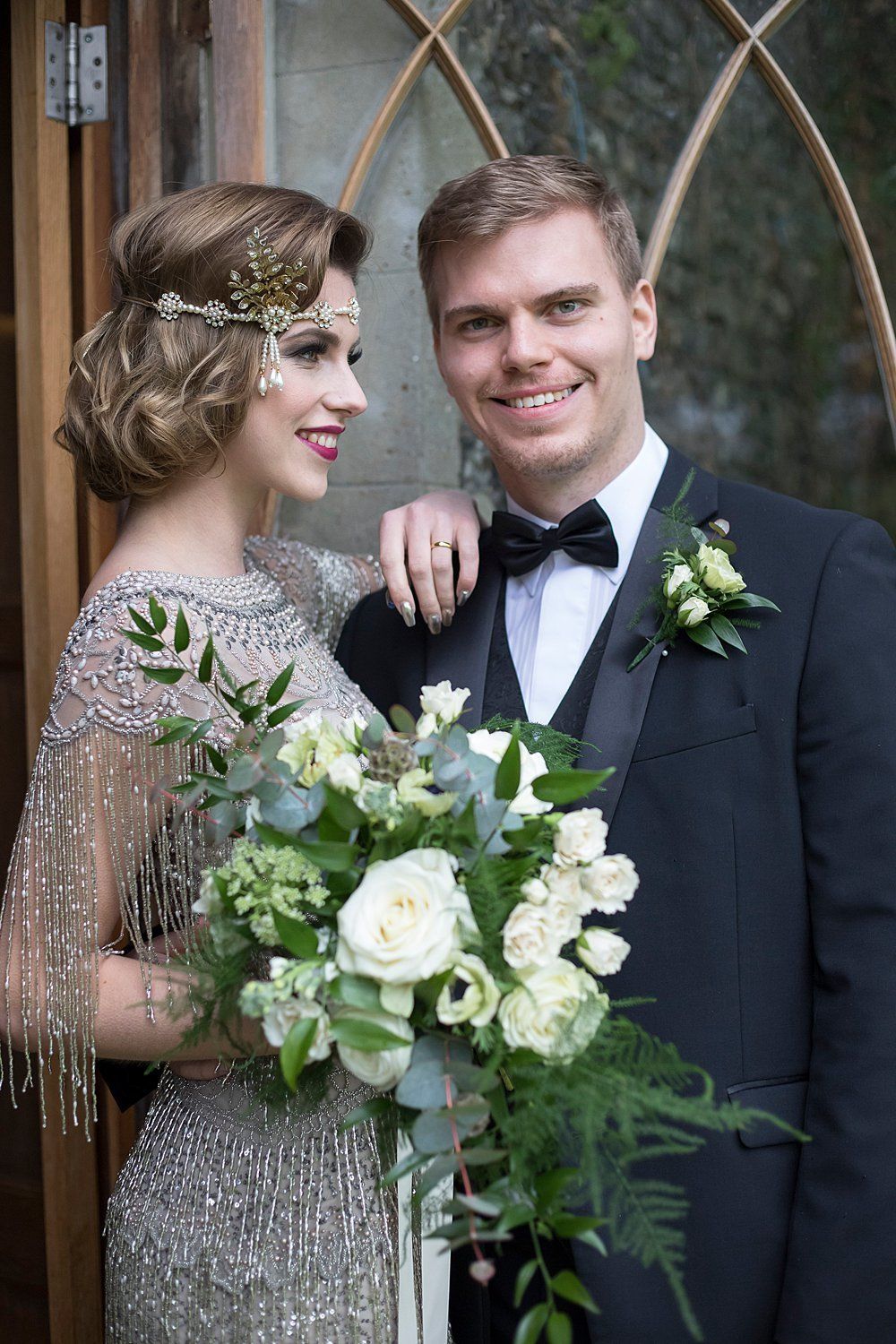 White bride and groom with bouquet standing smiling outside Nurstead Court
