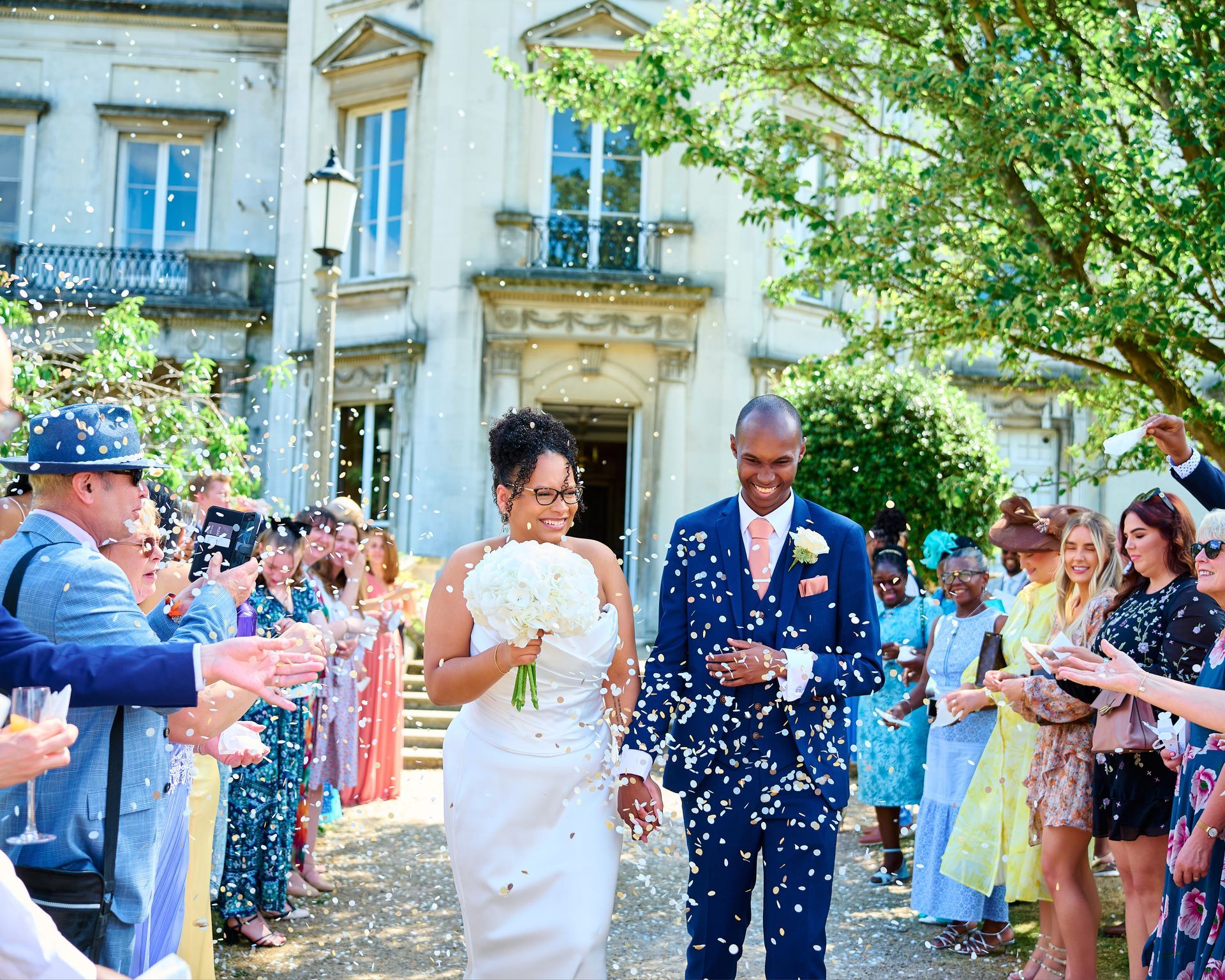 Bride and groom smiling and holdign hands walking through their confetti