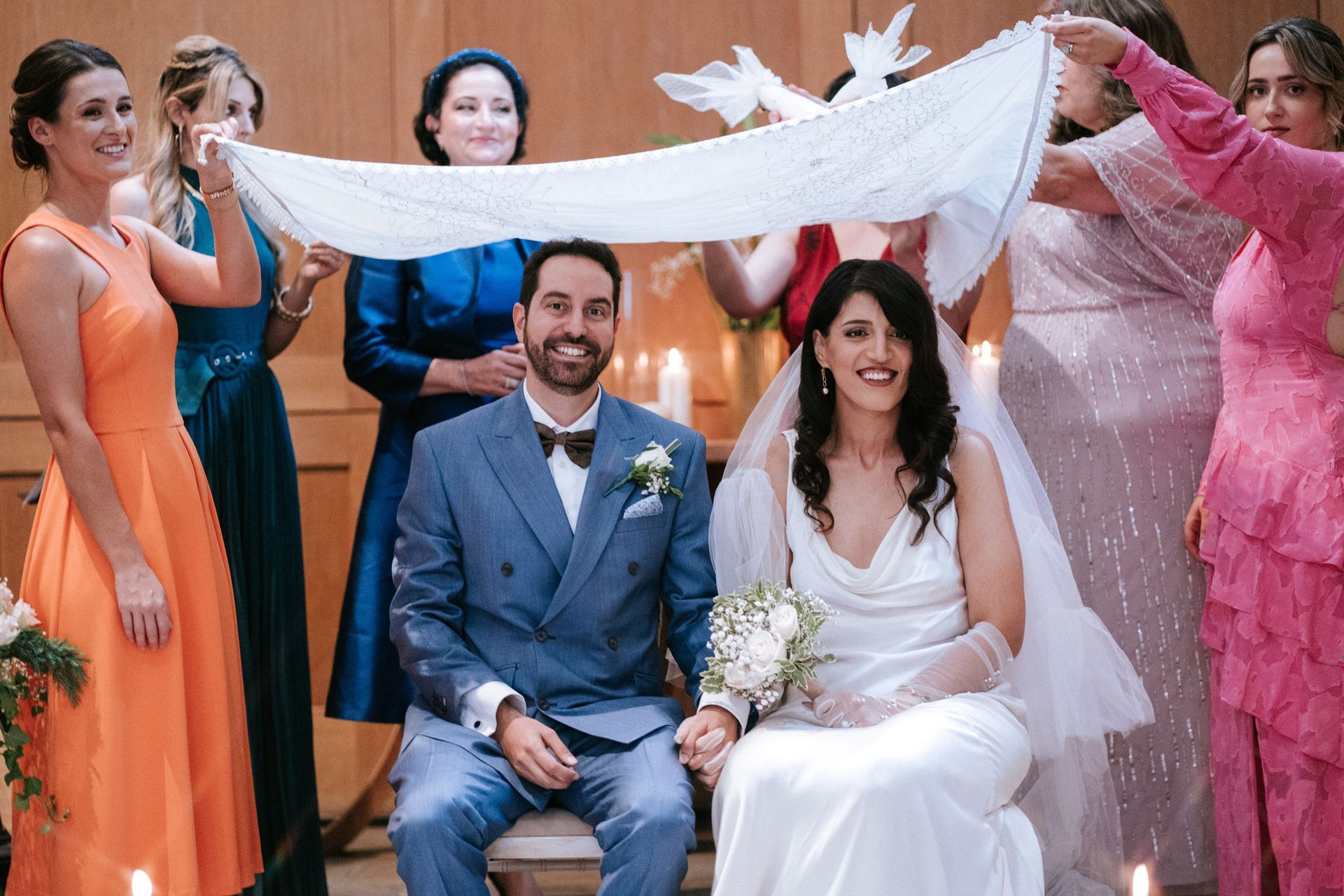 Bride & groom smiling, sitting at their Persian Wedding Sofrah Aghd with white fabric held over head