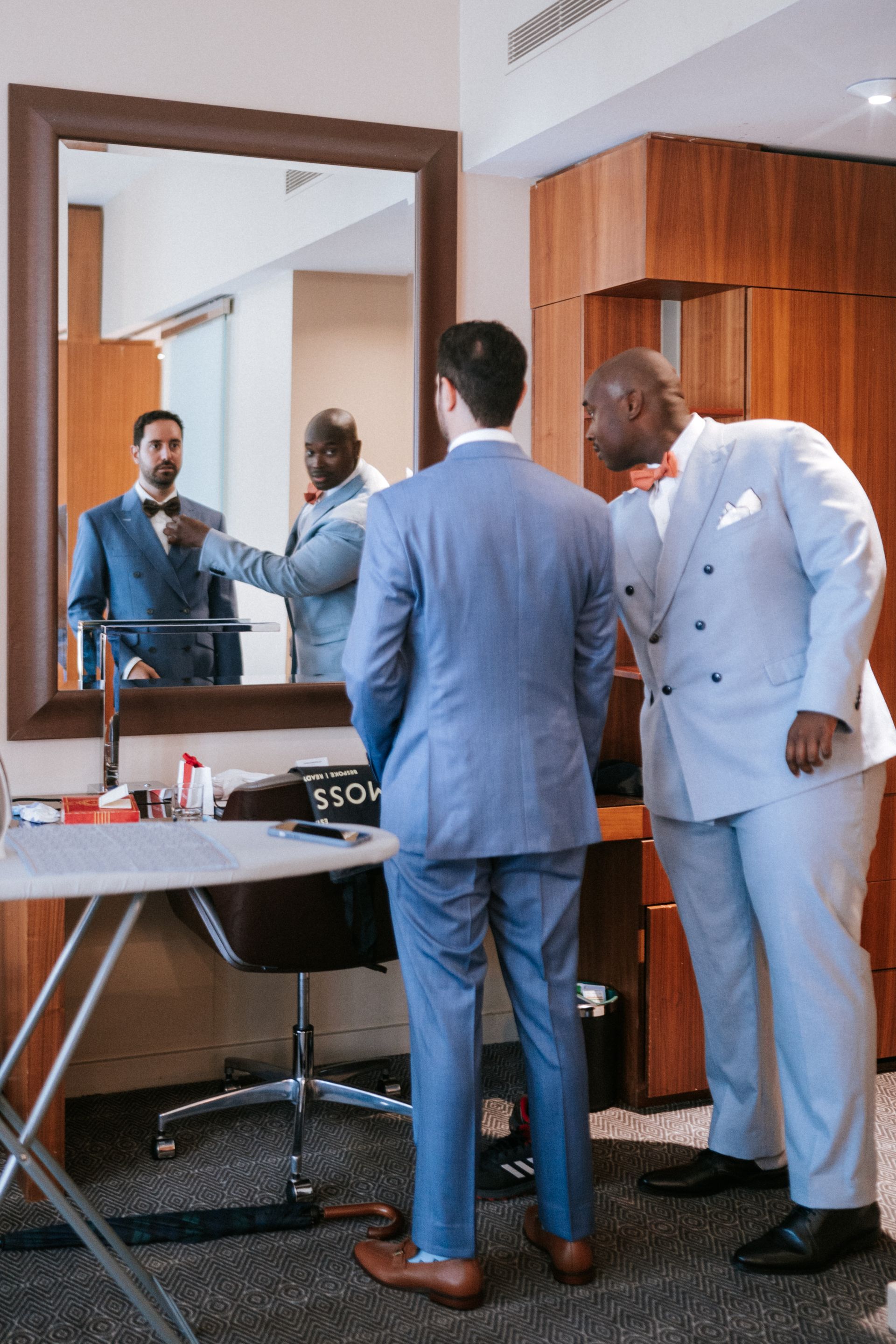 Groom in blue suit looking in a mirror with his best man