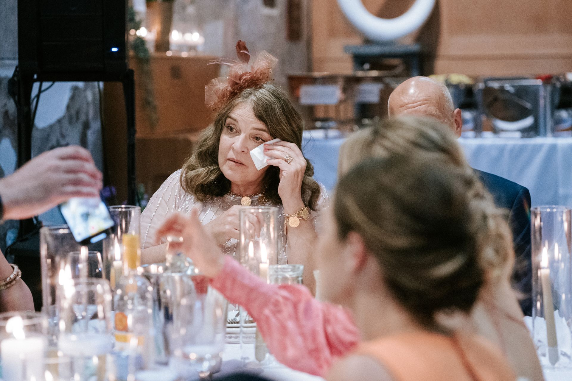 White woman seated at wedding table wiping tears from her eyes with a tissue