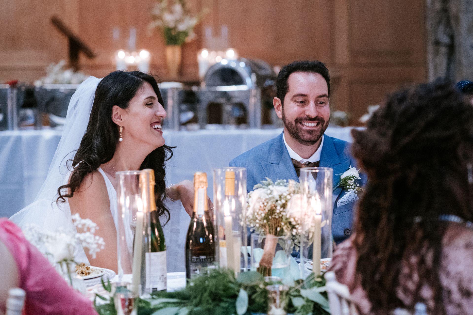 White bride and groom seated at wedding table with candles and smiling