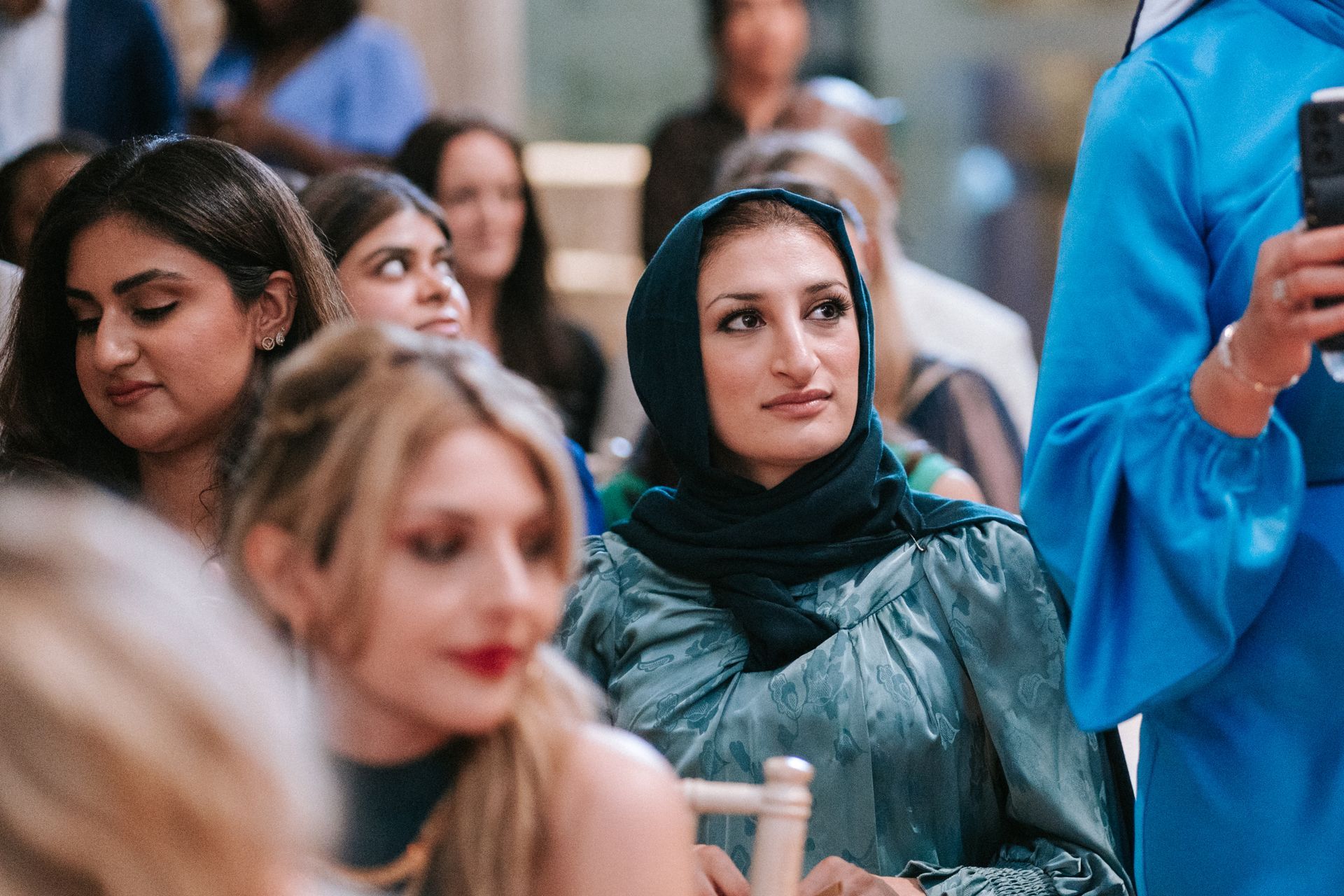 Woman seated at a wedding dressed in green with head covering