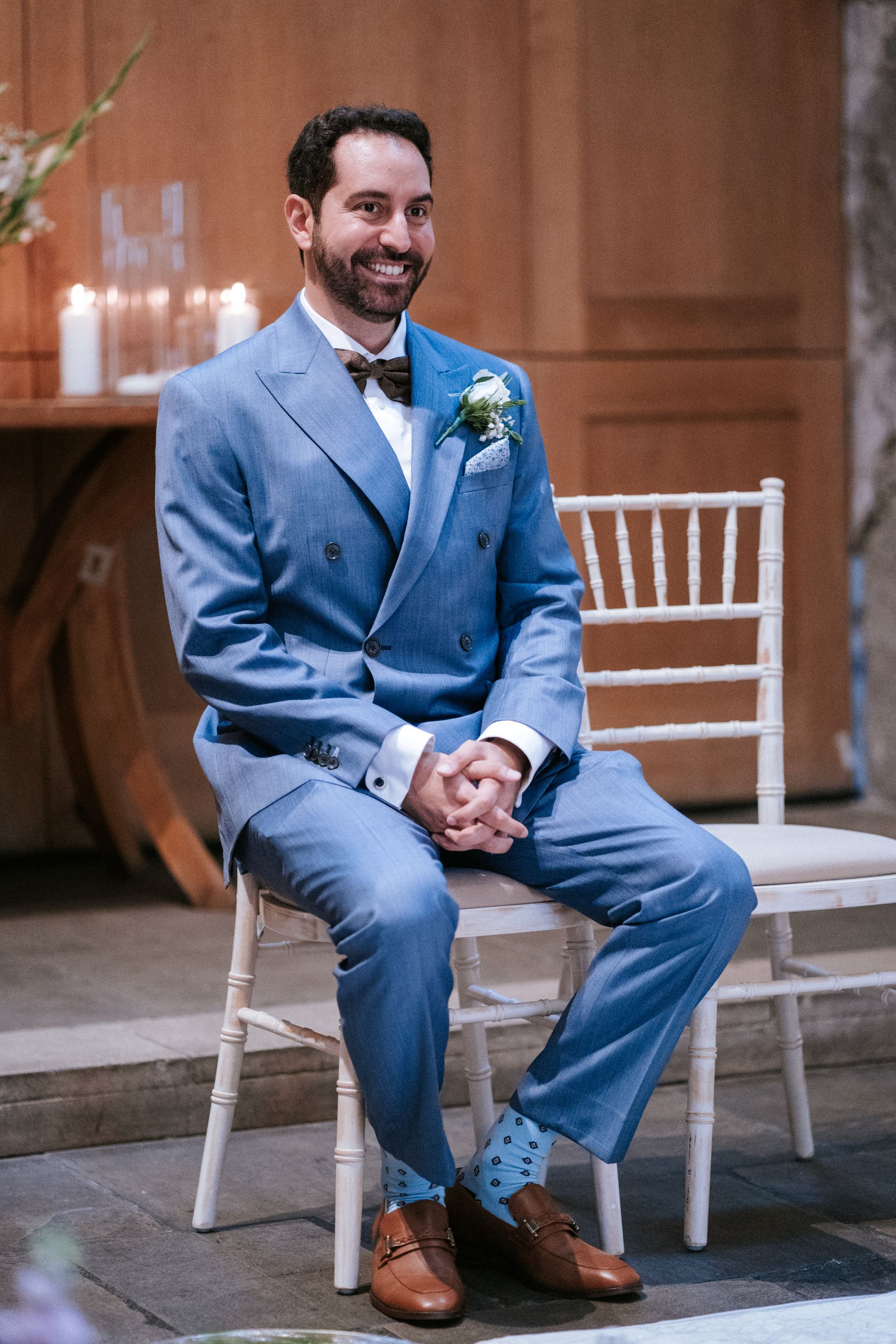 White groom in blue suit seated in a ceremony and clutching his hands