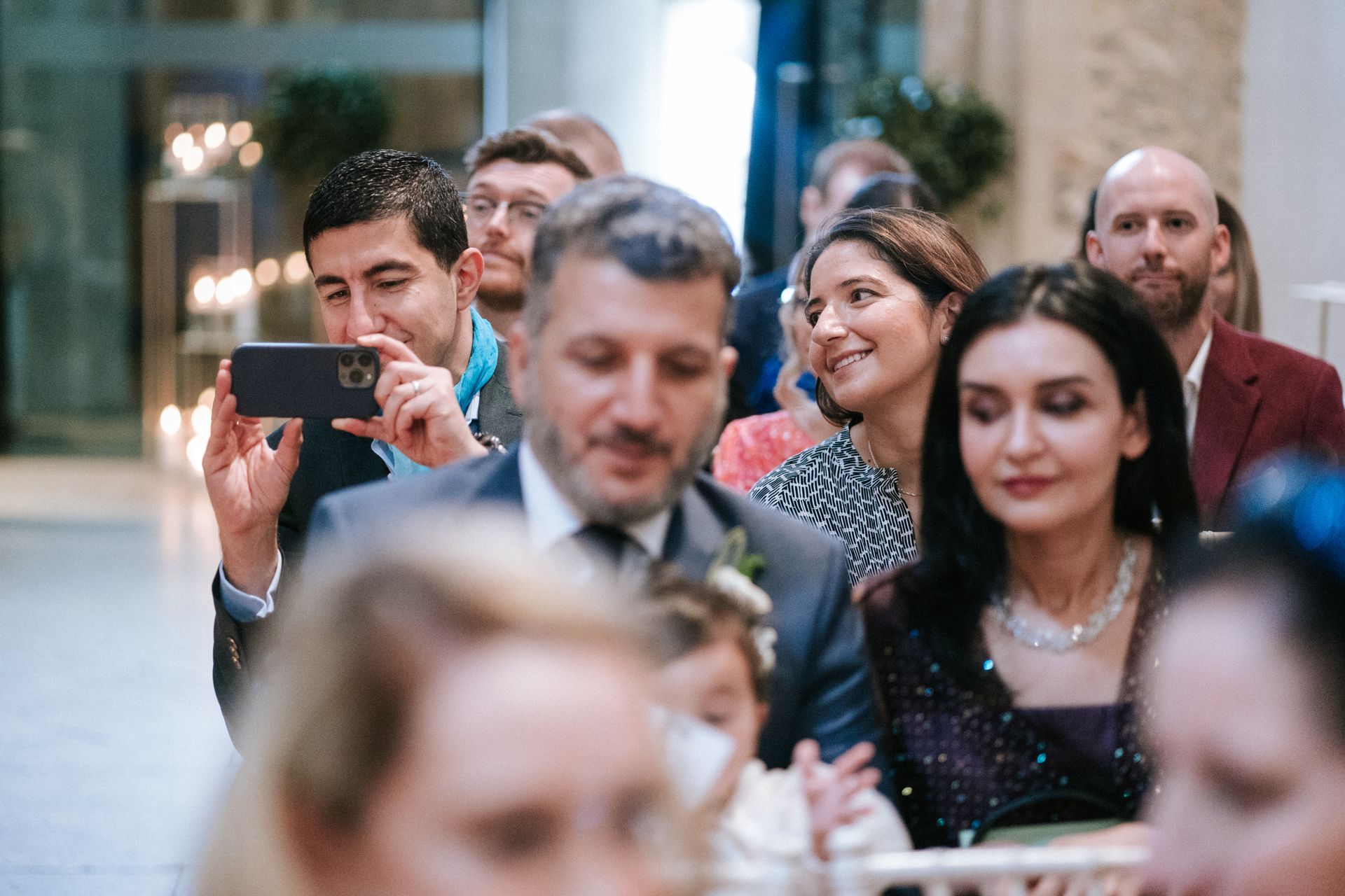 Wedding guests seated at a wedding ceremony taking photos on their phone