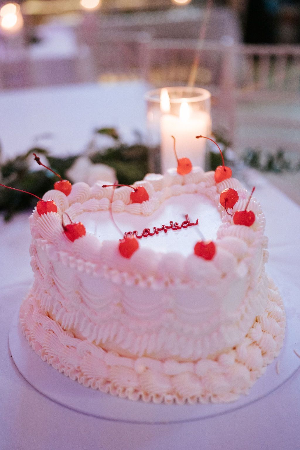 Heart-shaped white wedding cake with writing saying married decorated with red cherries