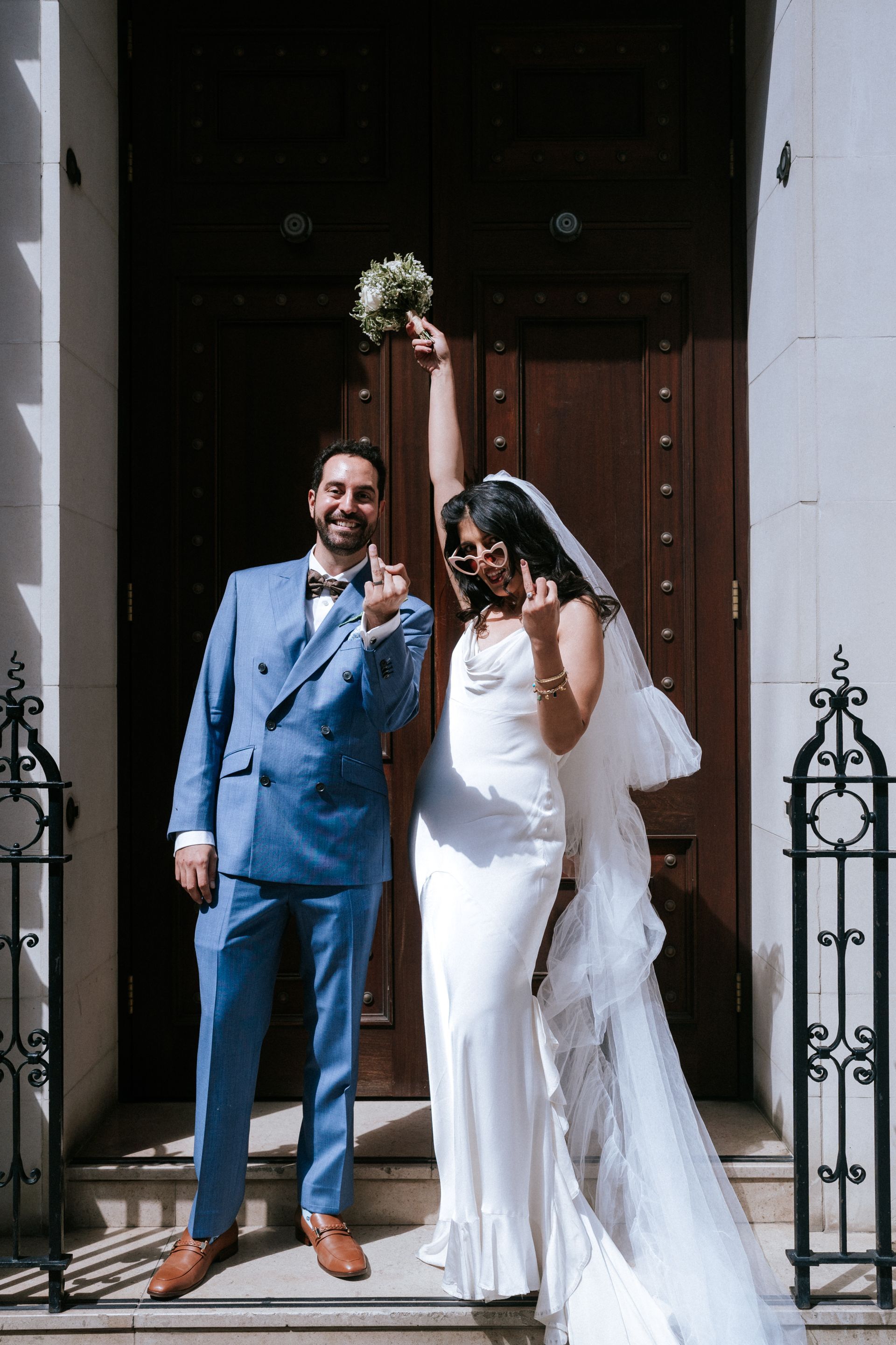 Bride and groom standing outside door with fingers up showing their wedding rings