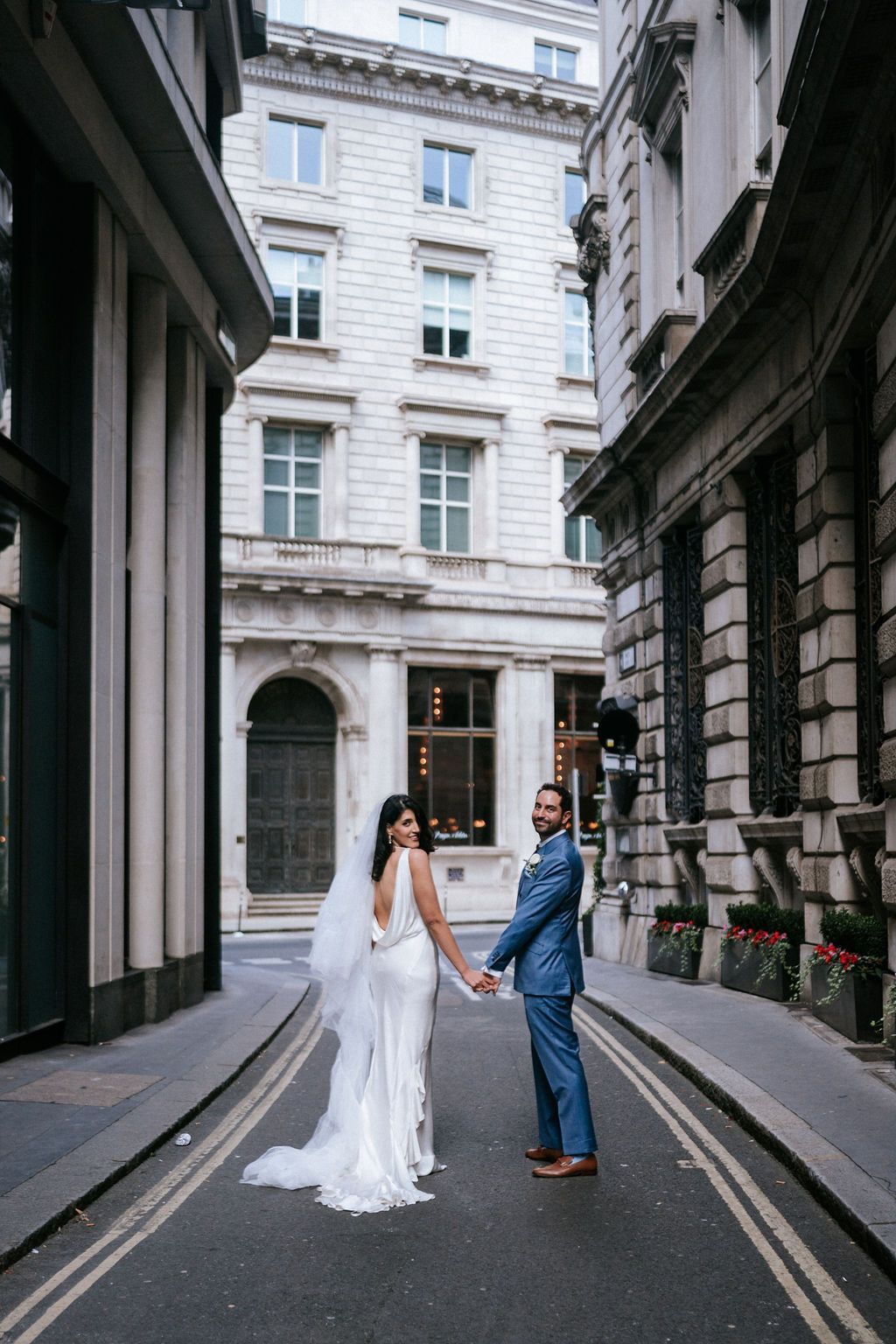 Bride and groom walking holding hands with back to camera. Walking down London City Road