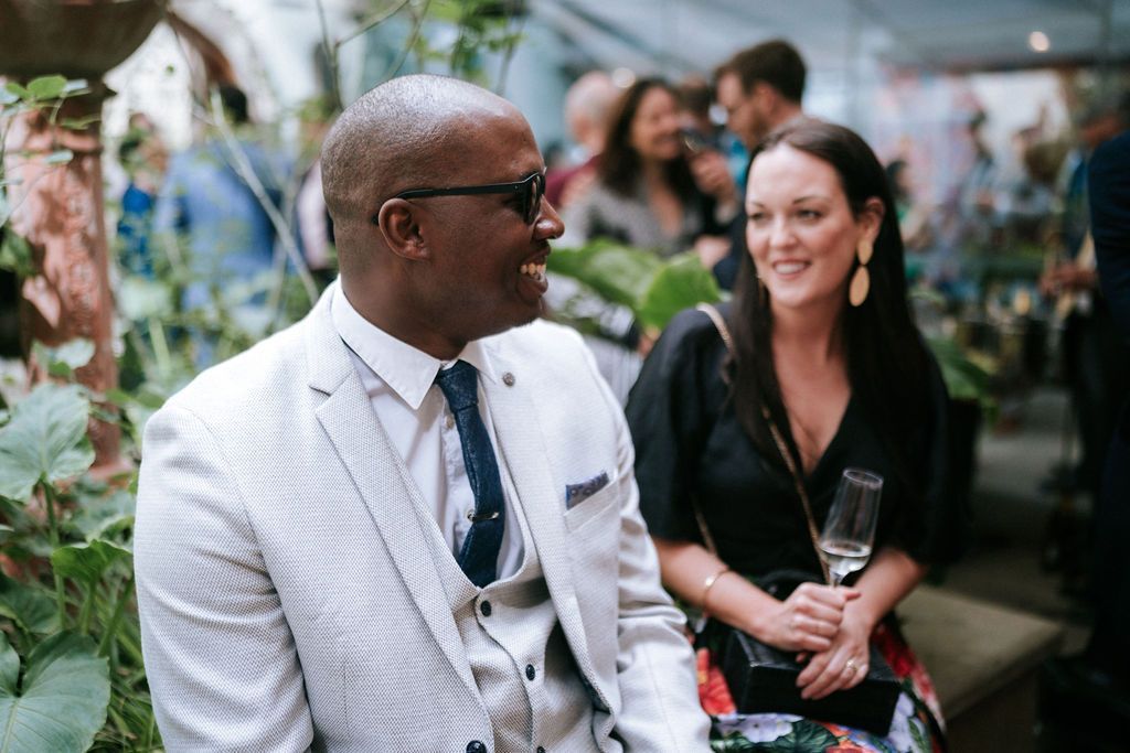 Black man seated and dressed in a light colour suite smiling at white woman in black top