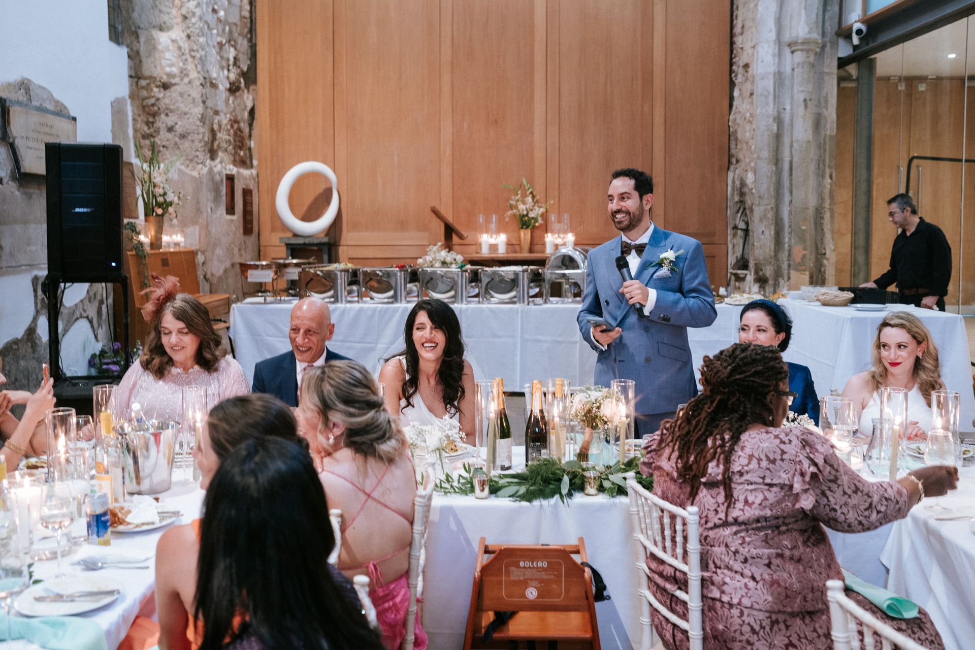 White man groom in blue suit standing at wedding table and giving a speech