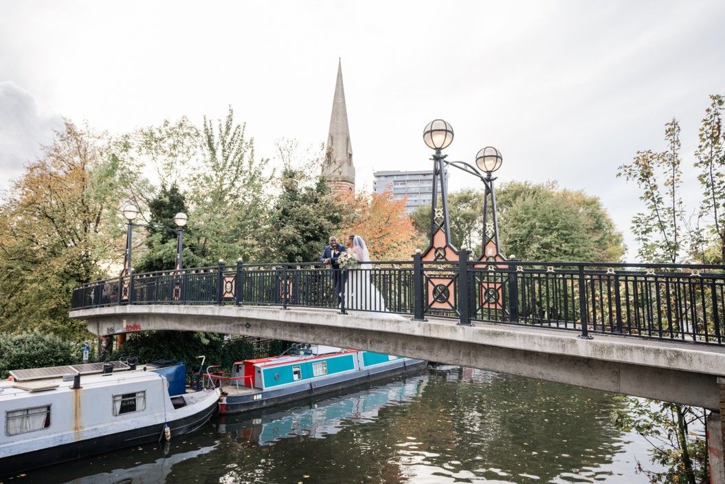 black bride and groom standing on bridge with canal in West London Madia Vale