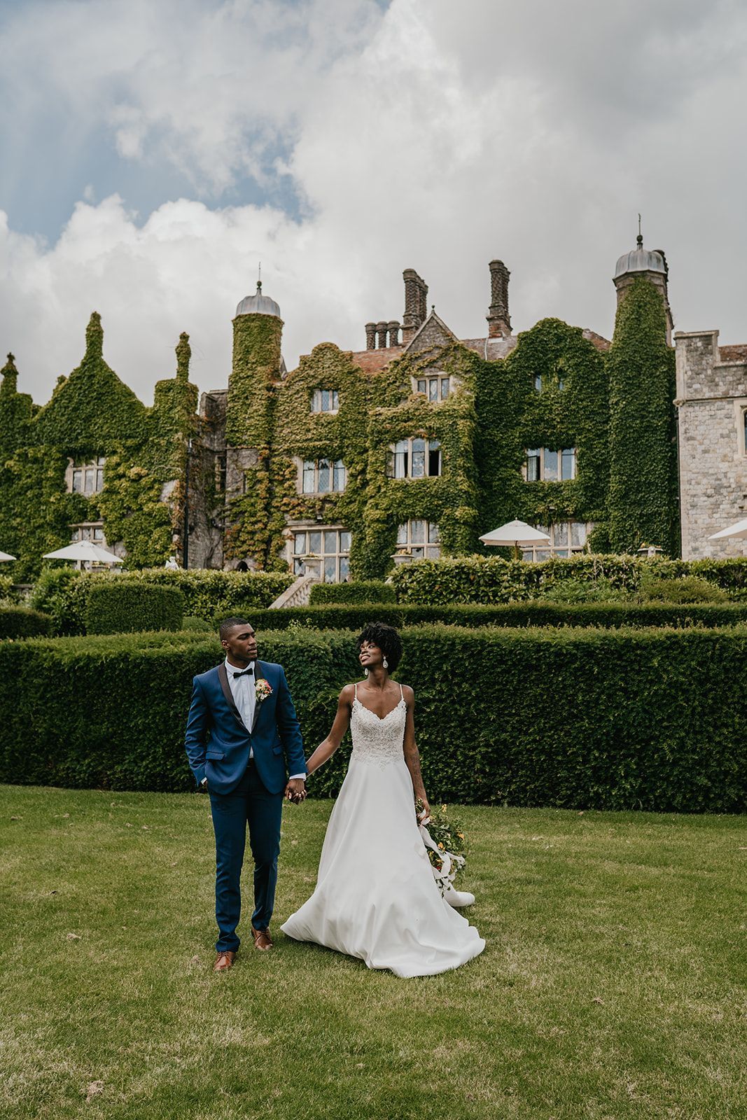 Black bride and groom holding hands and walking outside Eastwell Manor garden wedding