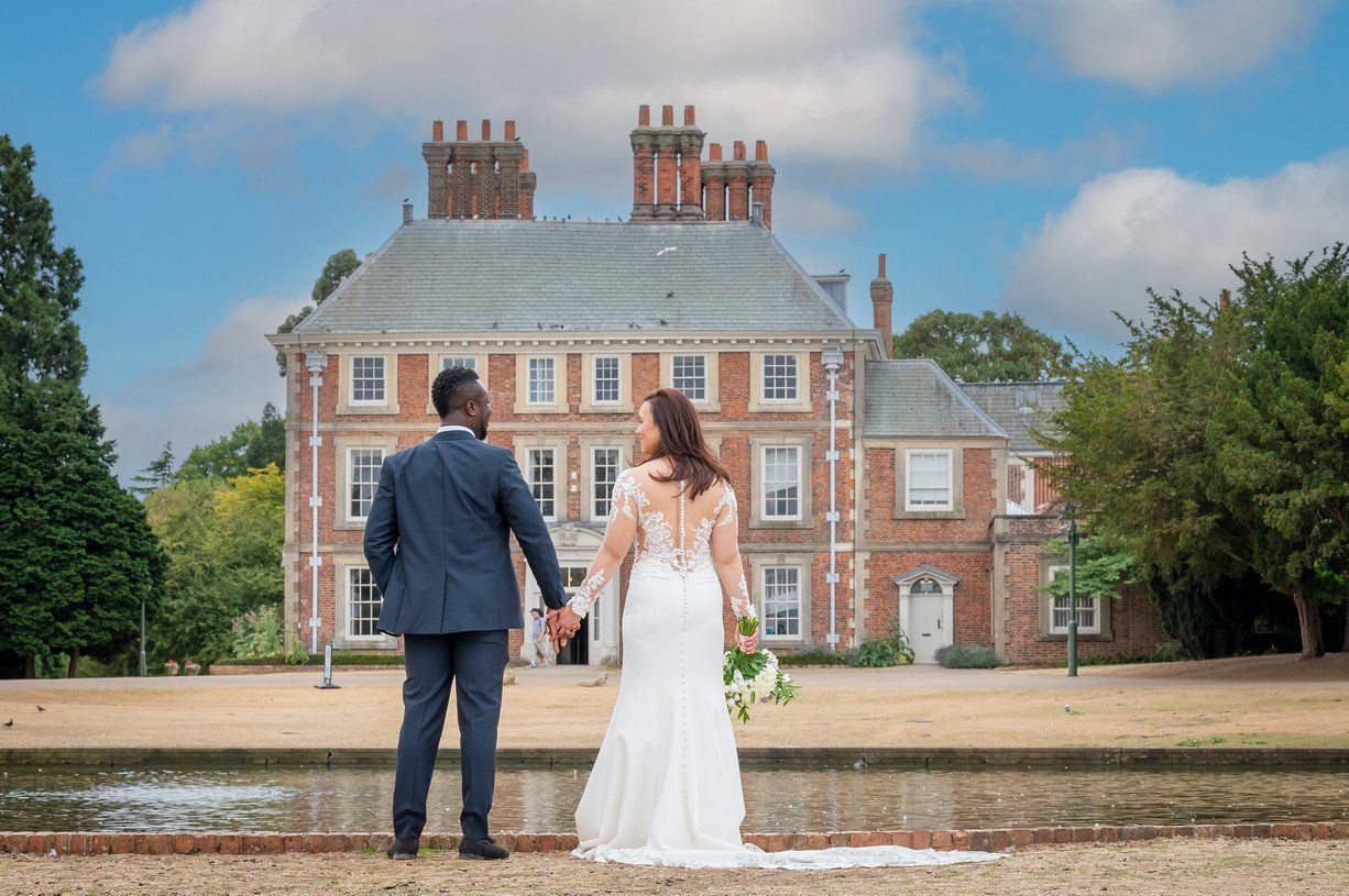 Bride and groom with backs to camera holding hands outside Forty Hall
