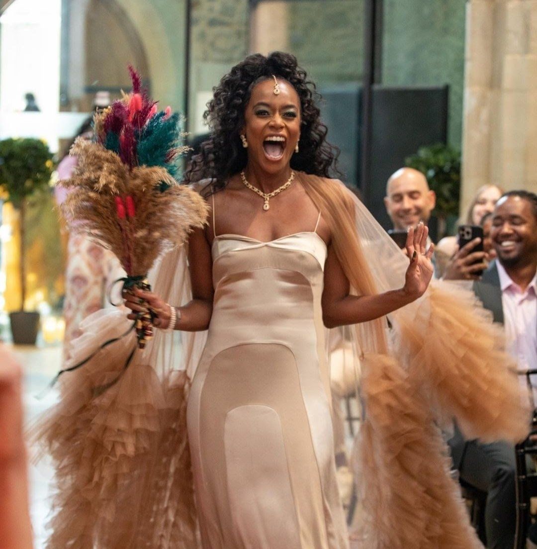 Joyful black bride wearing gold ruffled wedding dress walking down the aisle laughing