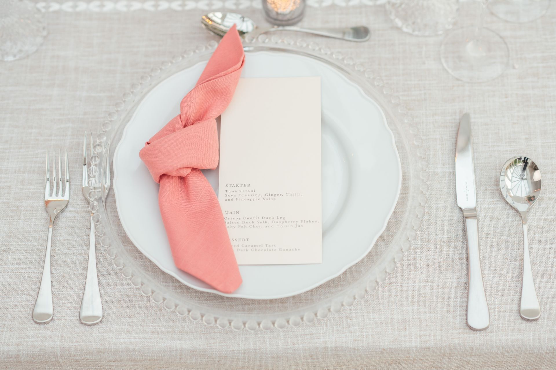 Clear glass beaded charger plate with white plate peach napkin knotted and blush pink menu