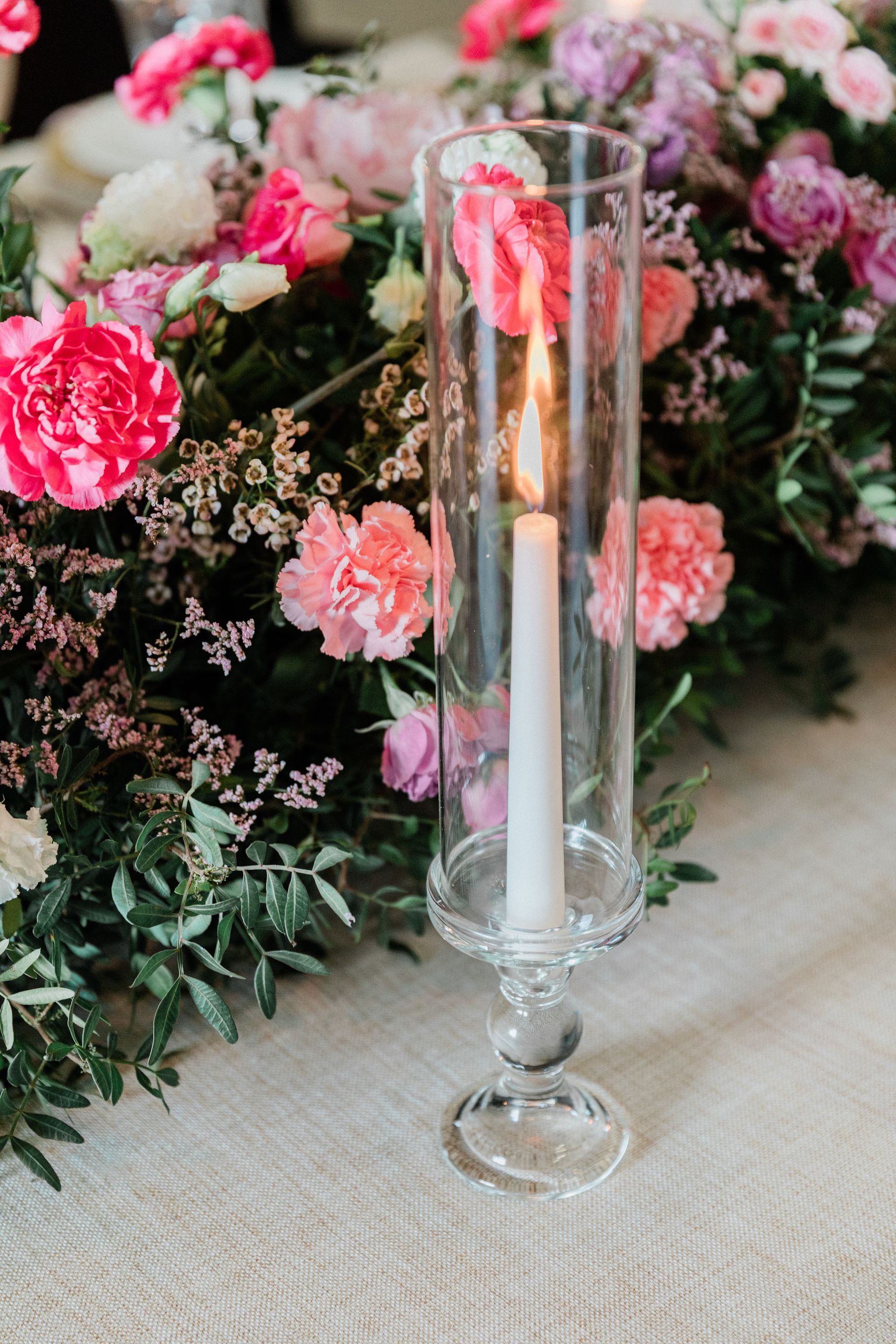 Crystal glass taper or pillar candle holder surrounded by pink flowers on a wedding table
