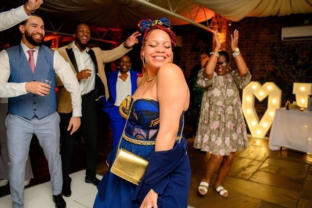 Mixed raced woman in blue african print dress dancing and smiling surrounded by guests who are smiling
