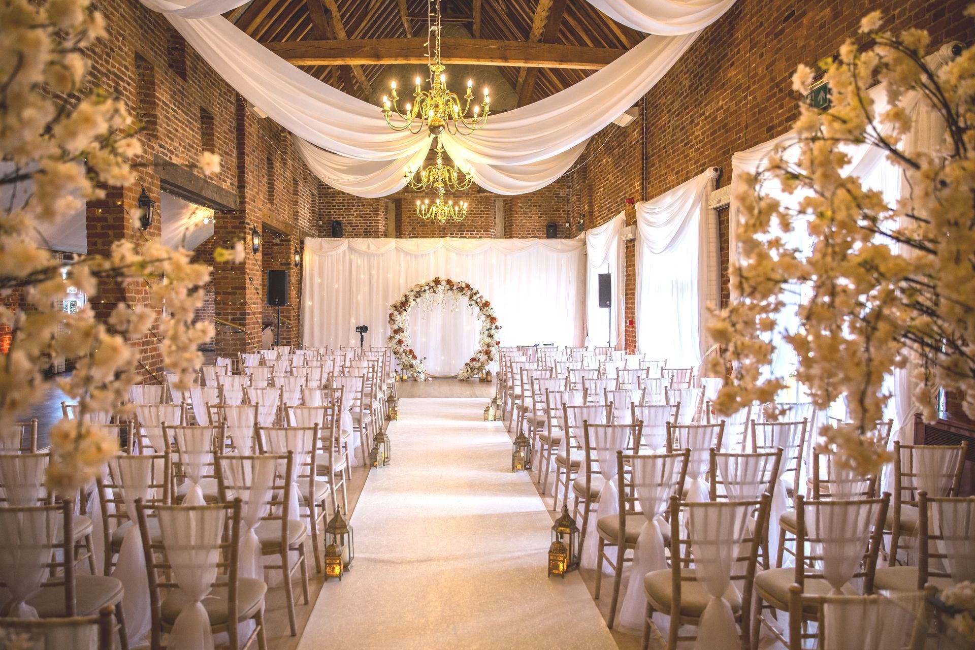 Forty Hall Banqueting Suite decorated with white aisle runner cream ceremony chairs and orange and cream flower circle ceremony backdrop