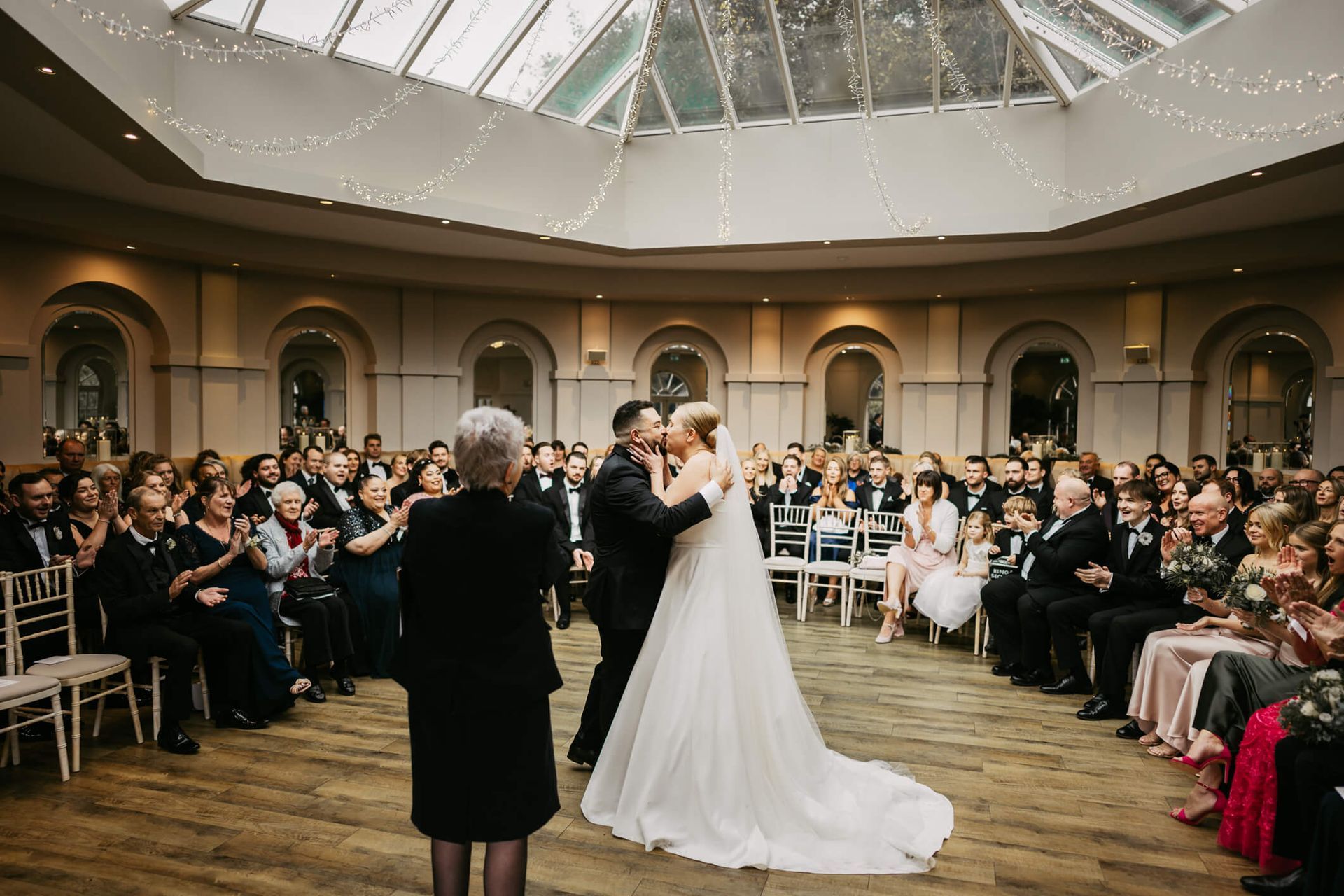 White bride and groom kissing in their wedding ceremony surrounded by their guests