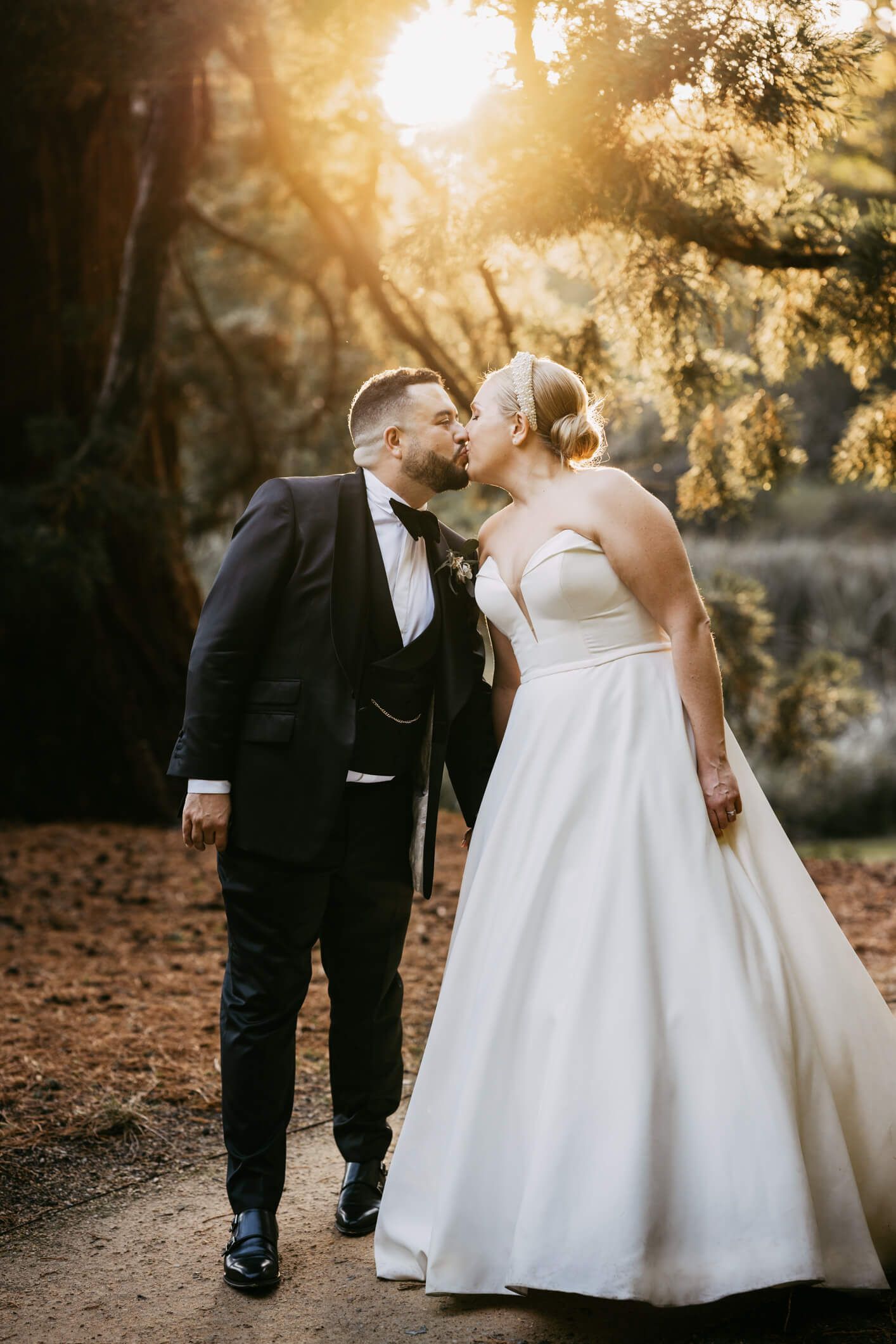 White bride and groom standing in the grounds of the Orangery Maidstone leaning into to each other to kiss with the sun setting in the background