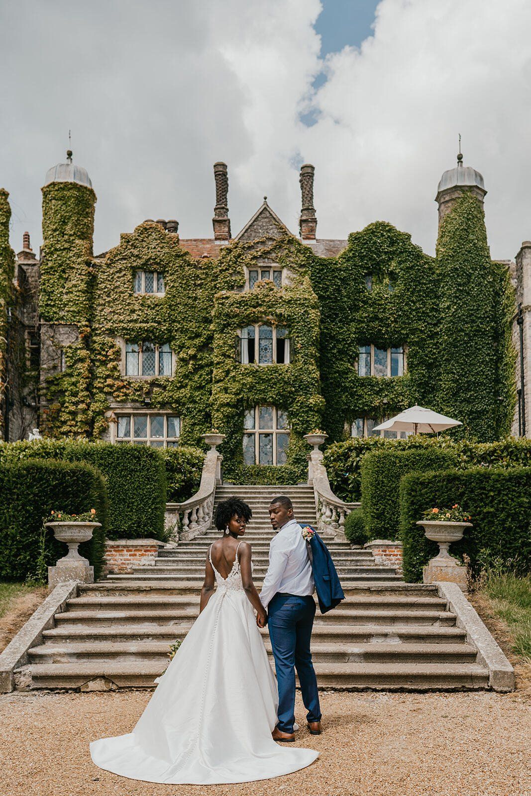 Black bride and groom holding hands outside Eastwell Manor with their backs to the camera