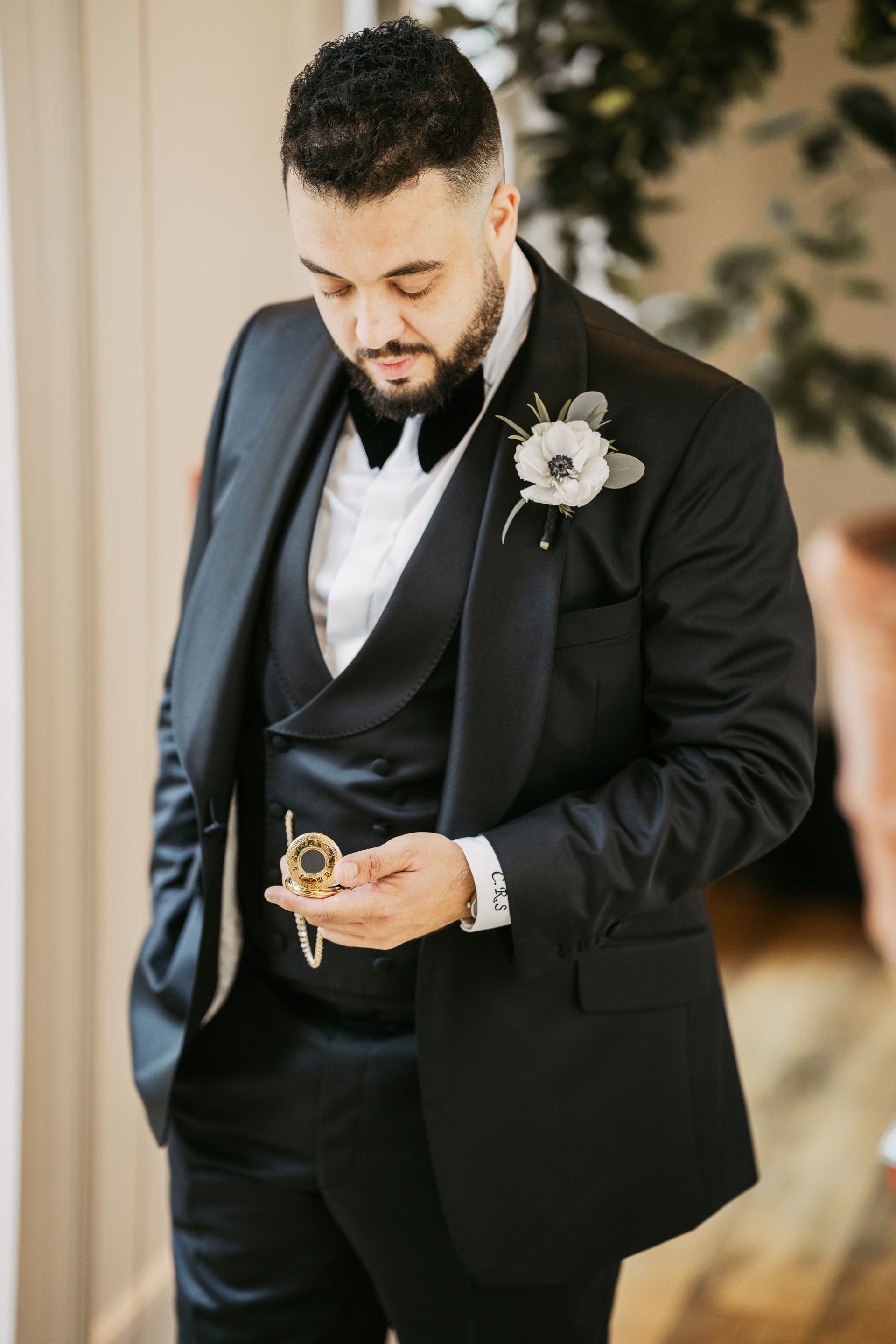White groom in black tuxedo looking at gold pocket watch