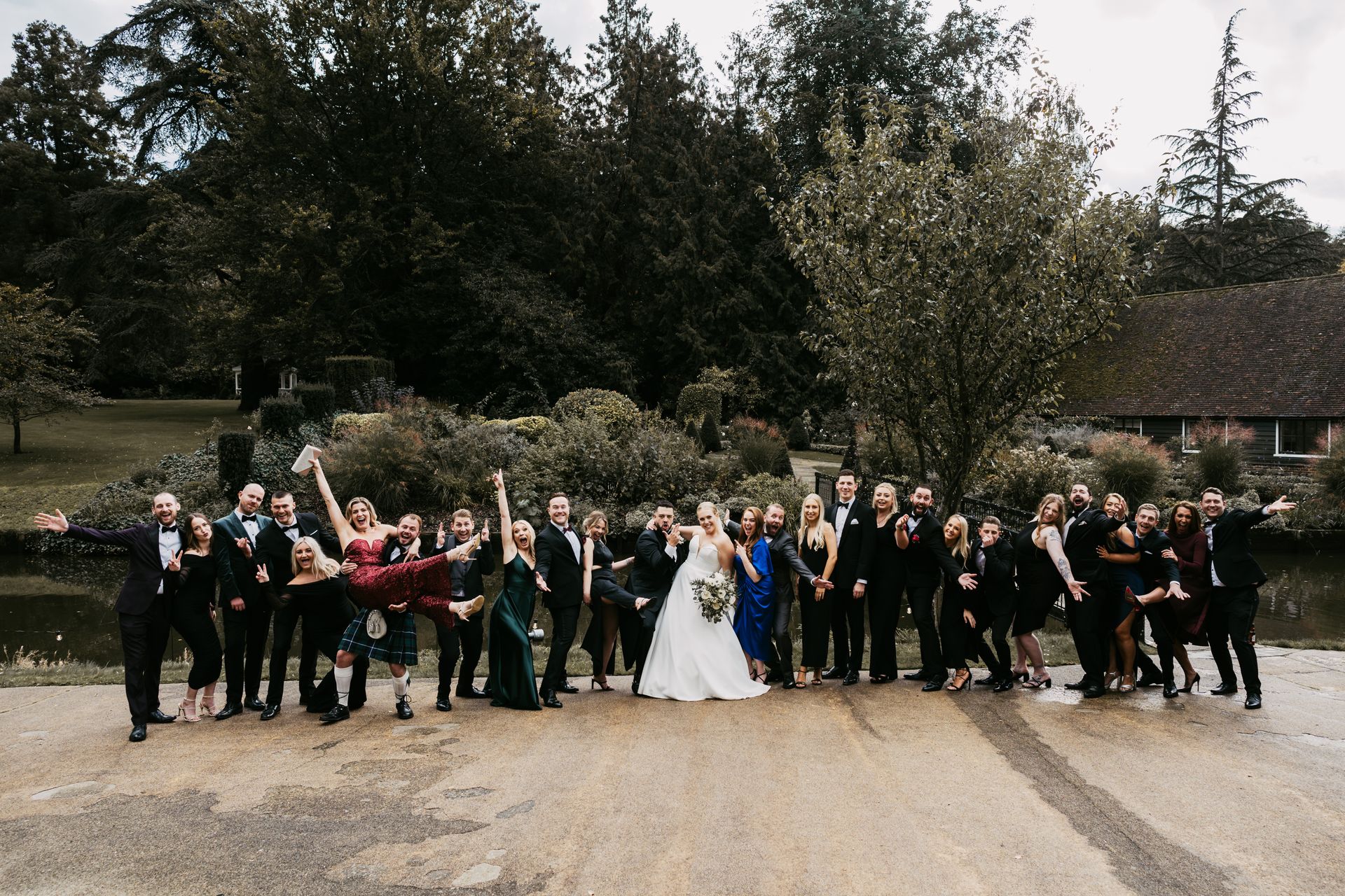 Group of wedding guests in evening attire making poses as they stand with bride and groom