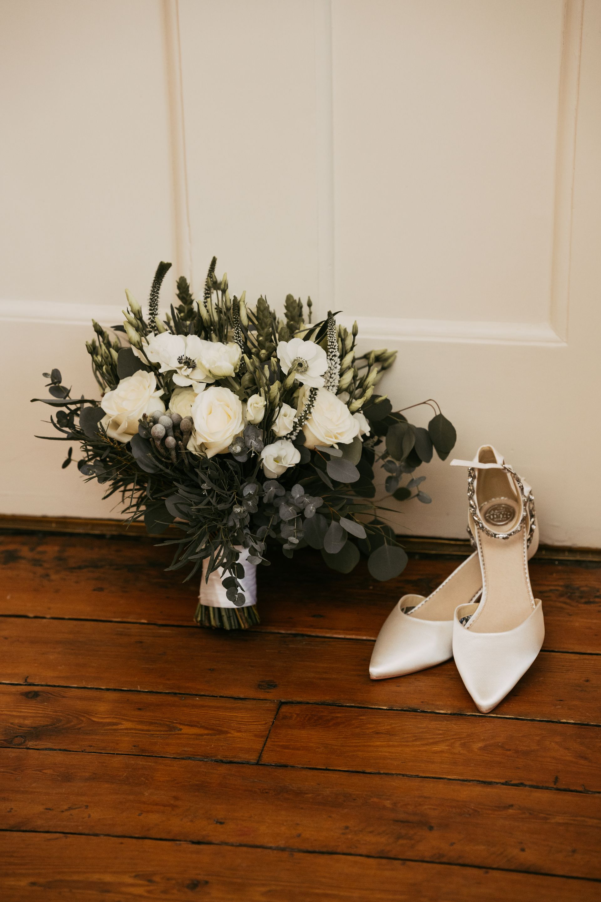 White and green brides bouquet displayed next to cream pointy bridal shoes