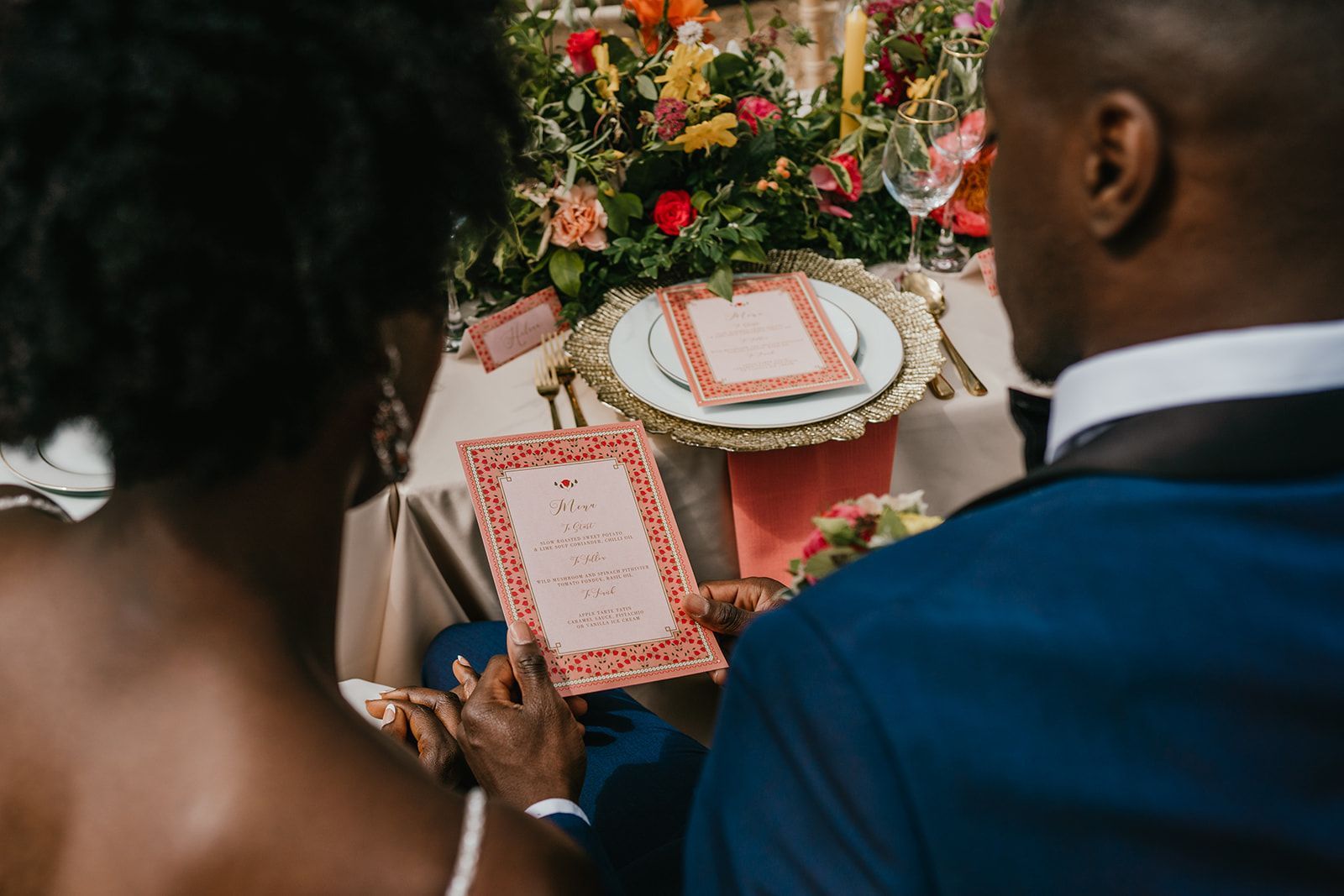 Colourful orange and peach wedding stationery set up in garden with bride and groom reading the menu