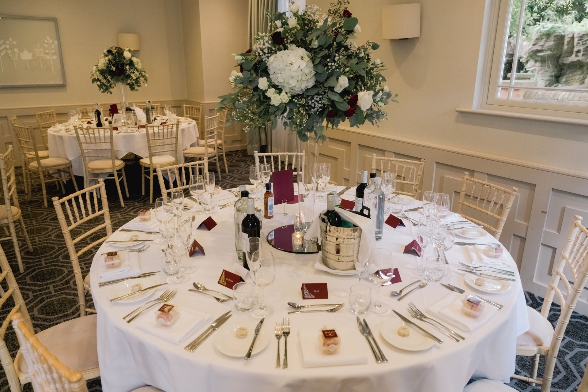 Wedding reception round table decorated with red and cream flowers and deep red placecards