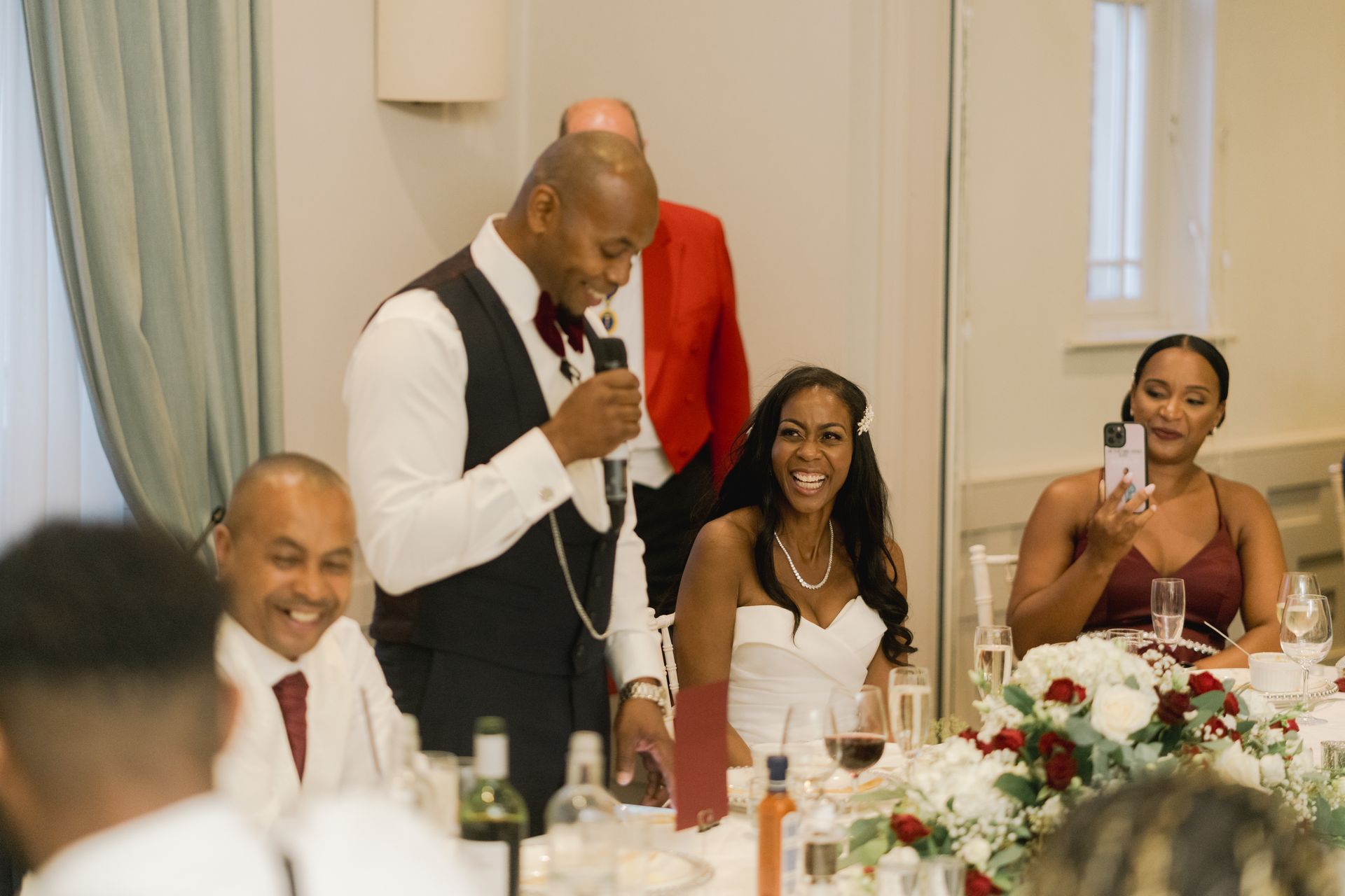 Black groom standing and giving speech as bride looks on smiling