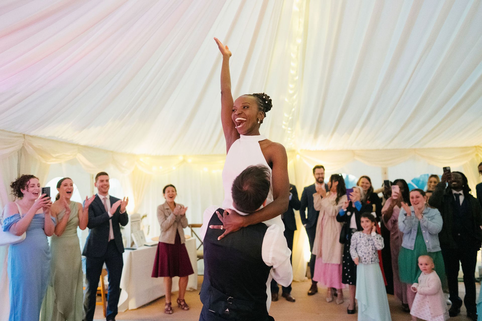 Afro-French wedding bride has been lifted by the groom on the dancefloor with her hand in the air.