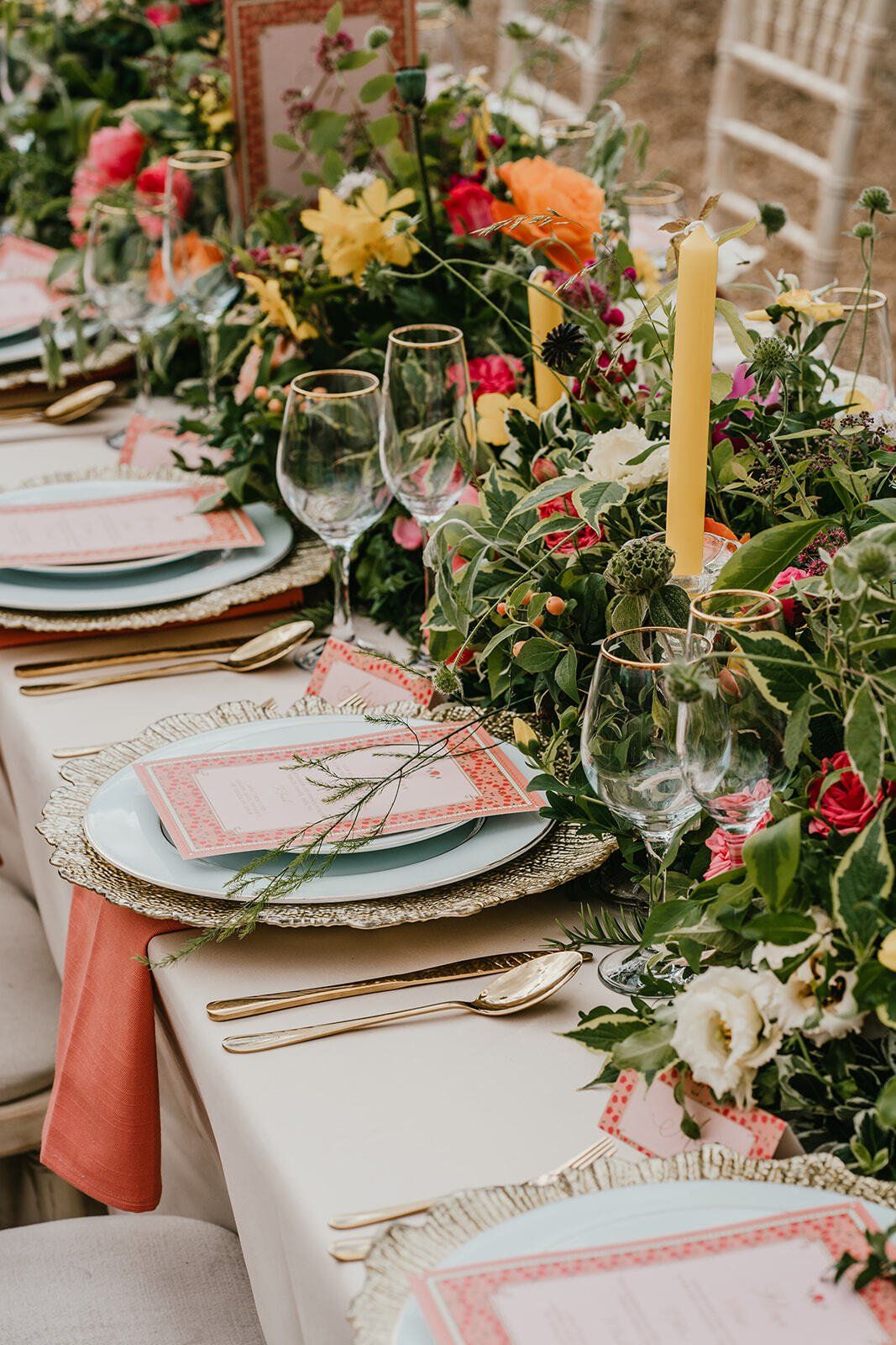 Elegant and colourful outdoor Wedding table set up with gold charger plates foliage flowers runner and peach napkins