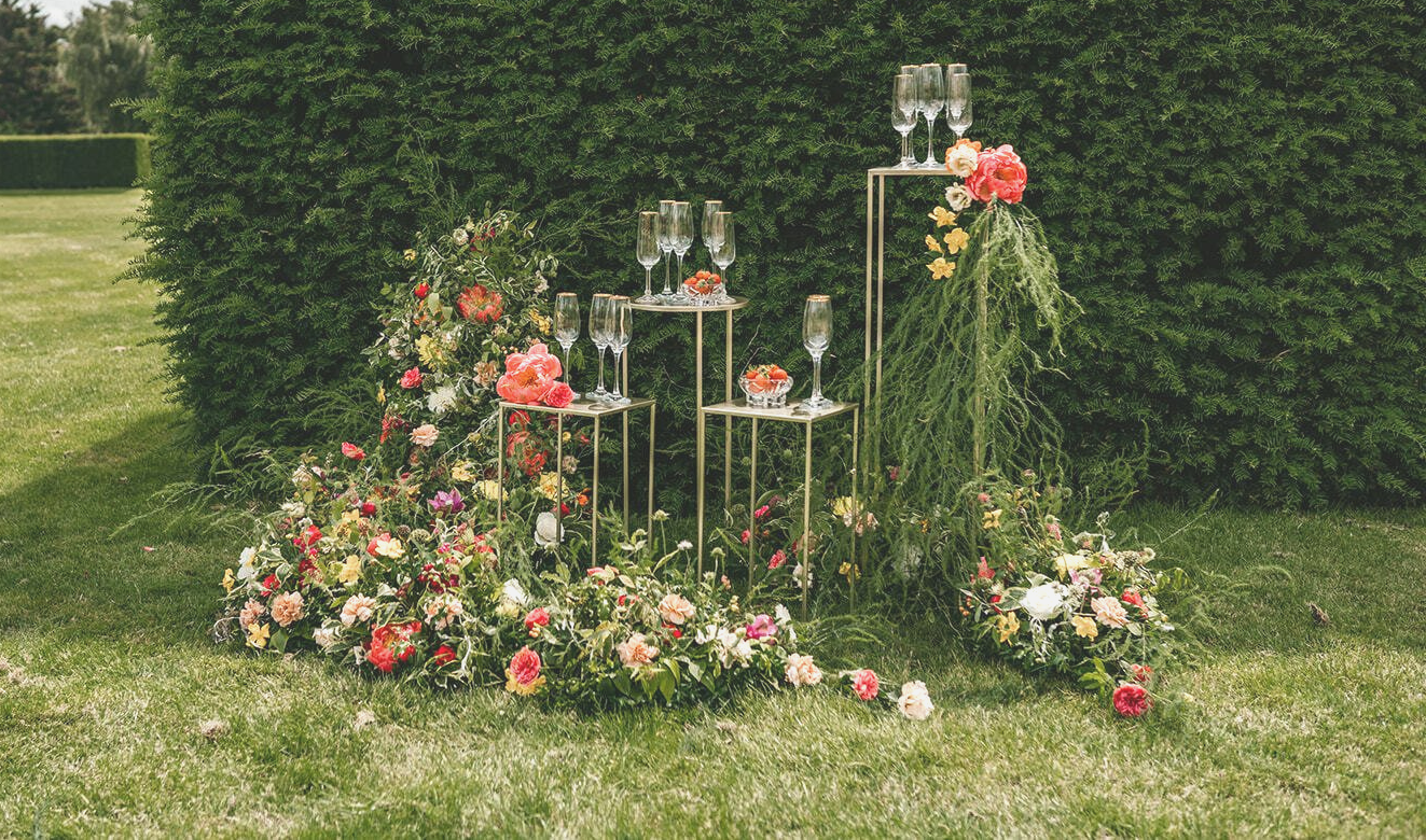 Set of gold pedestals displayed with flowers and champagne outside on a lawn