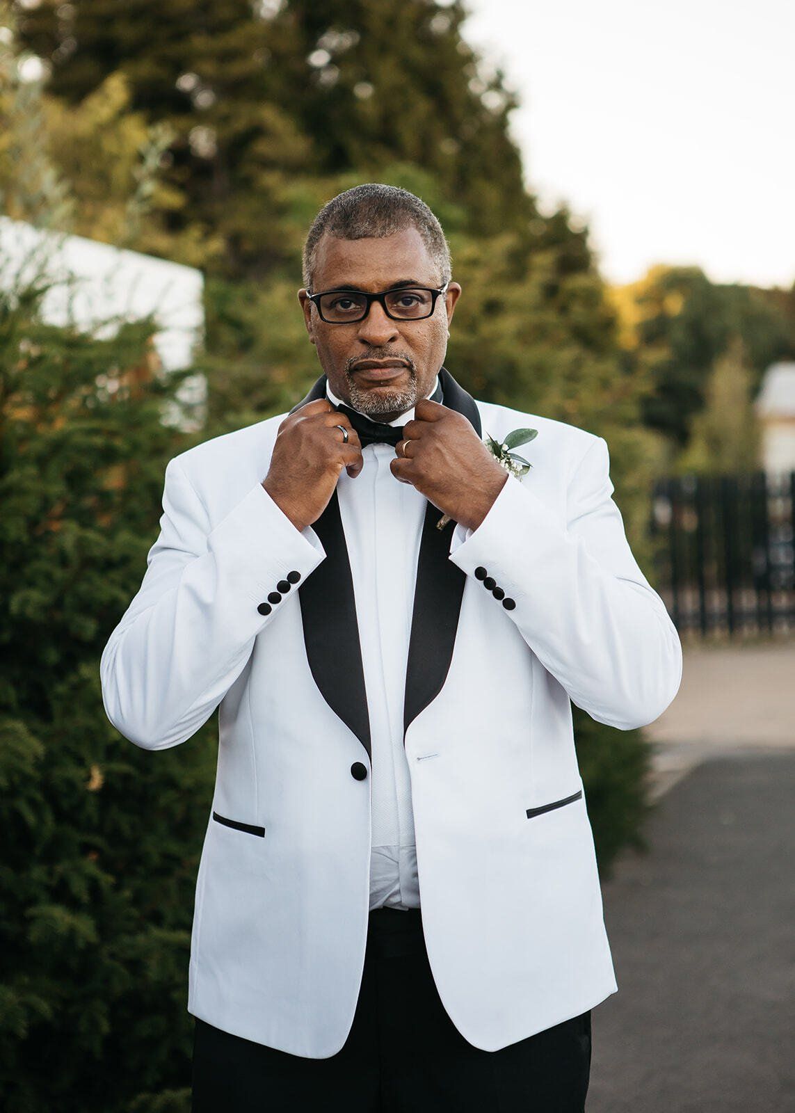 Black groom holding onto his black bowtie looking at camera