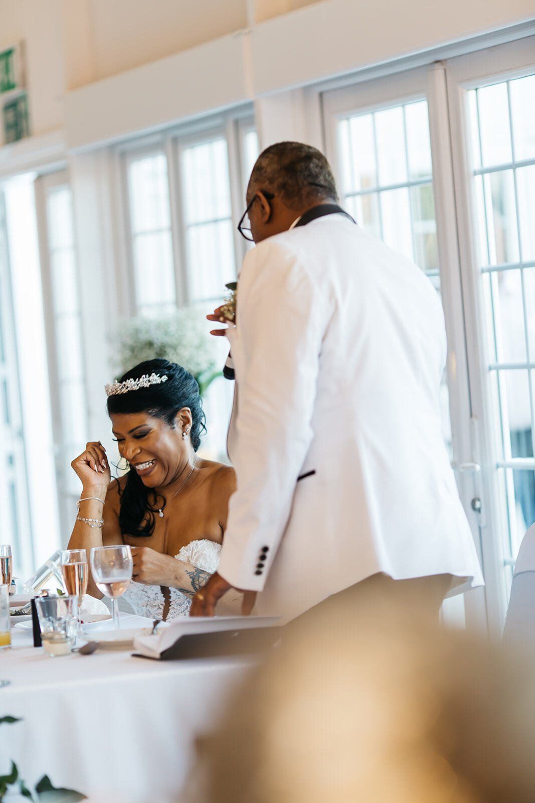 Groom standing and speaking to his bride and bride seated smiling