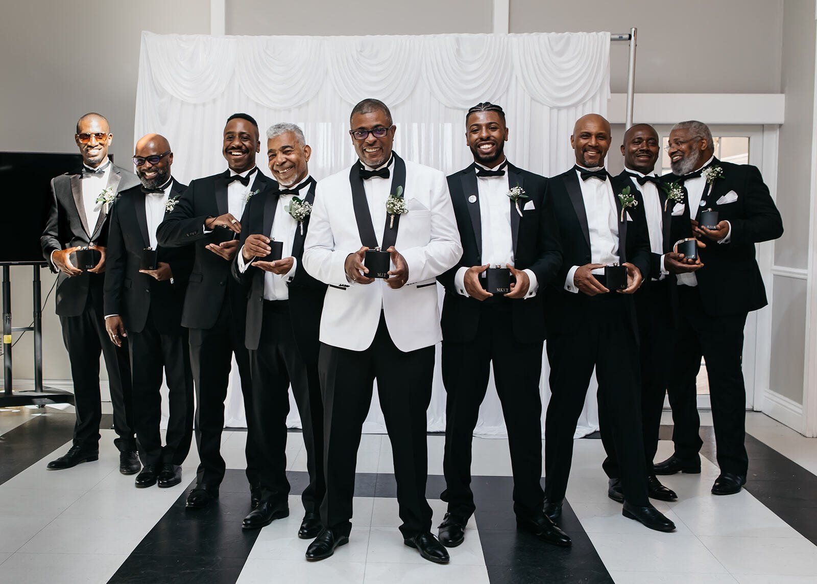 8 black groomsmen in black and white tuxedos standing posing